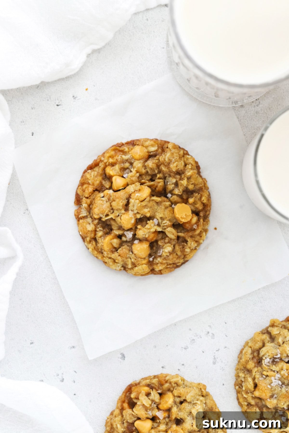 A close-up view of a baked gluten-free oatmeal scotchies cookie with visible butterscotch chips and a sprinkle of sea salt.