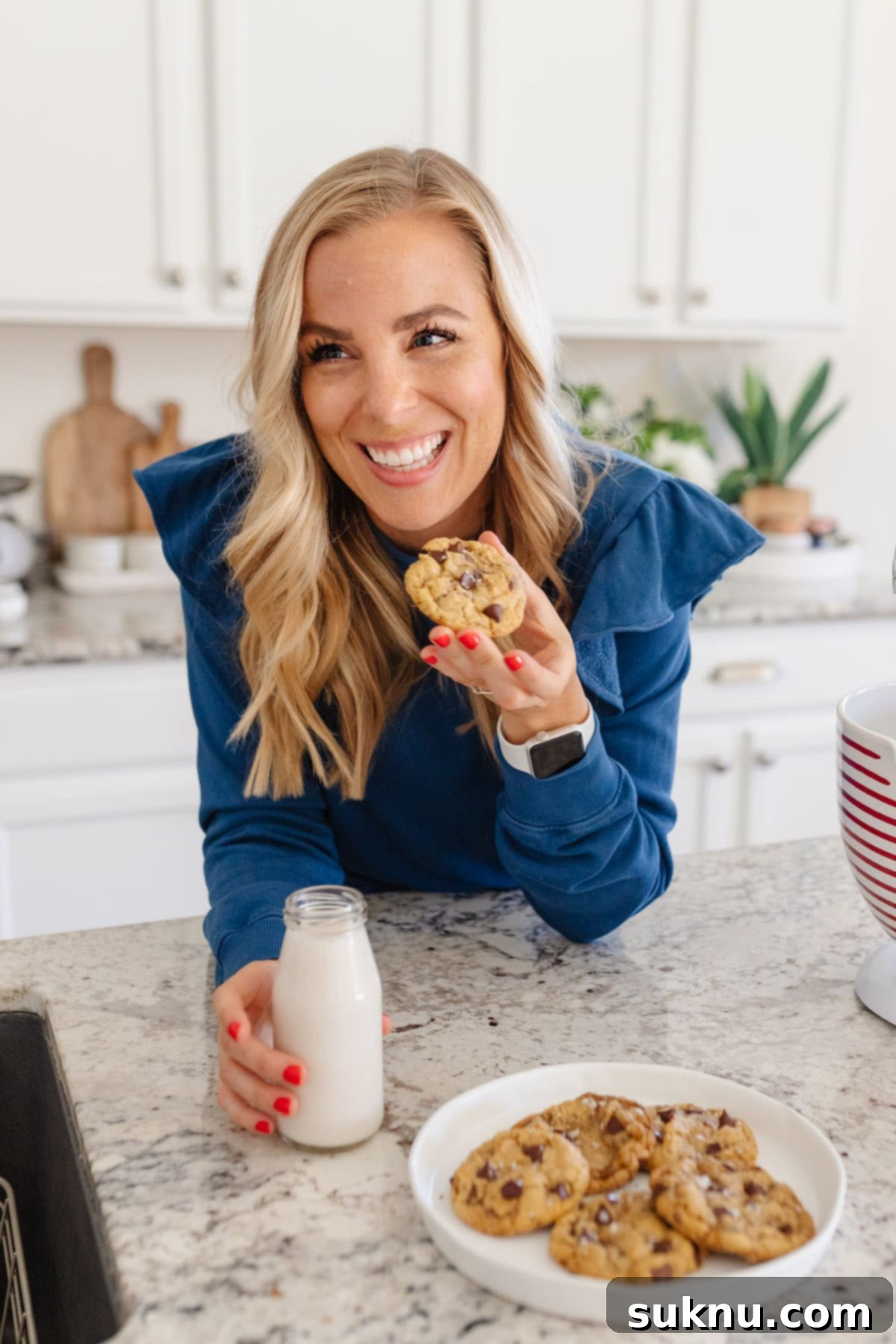 Emily Dixon from Sweets And Thank You in her kitchen eating a gluten-free cookie with almond milk