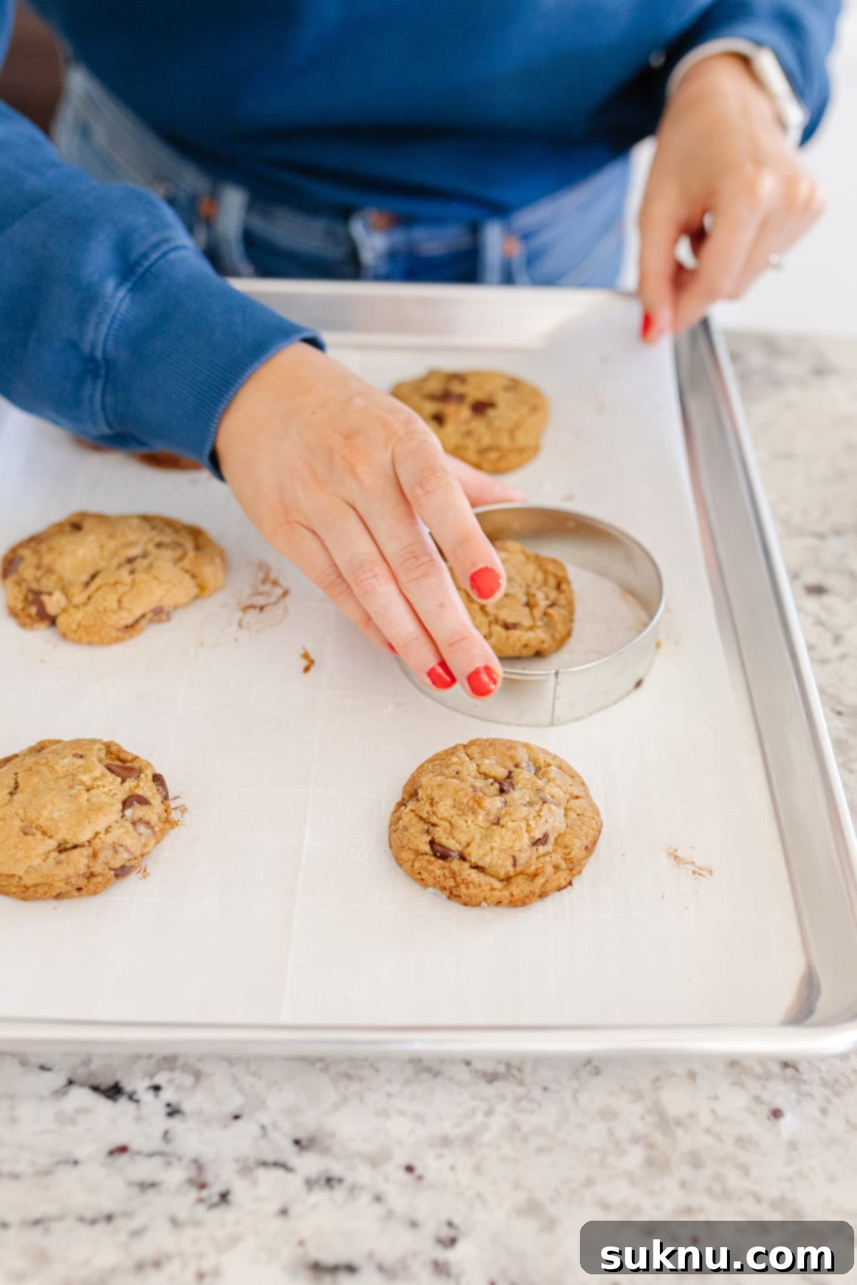 Using a large circular cookie cutter to shape freshly baked cookies into circles