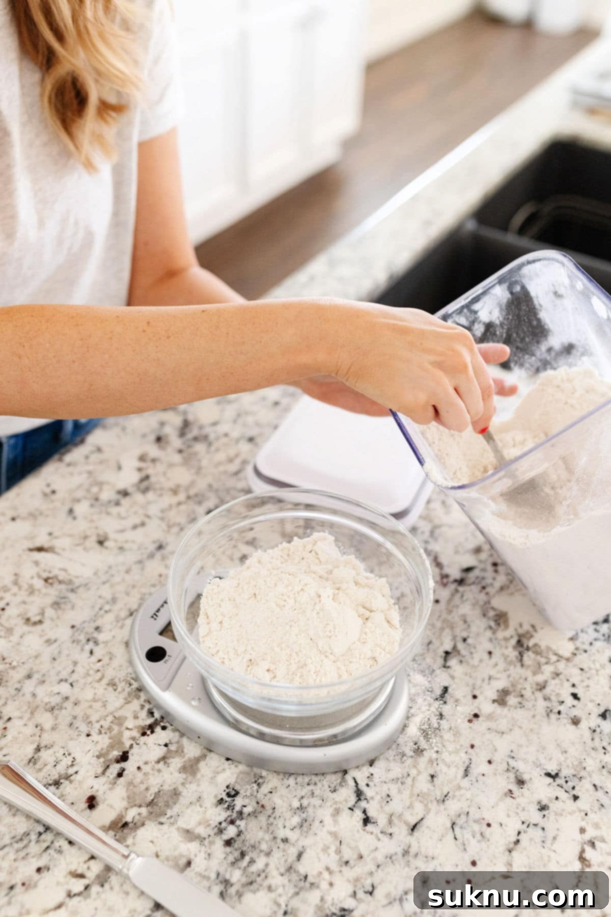 Emily Dixon from Sweets & Thank You scooping gluten-free flour into a glass bowl on a kitchen scale to weigh it