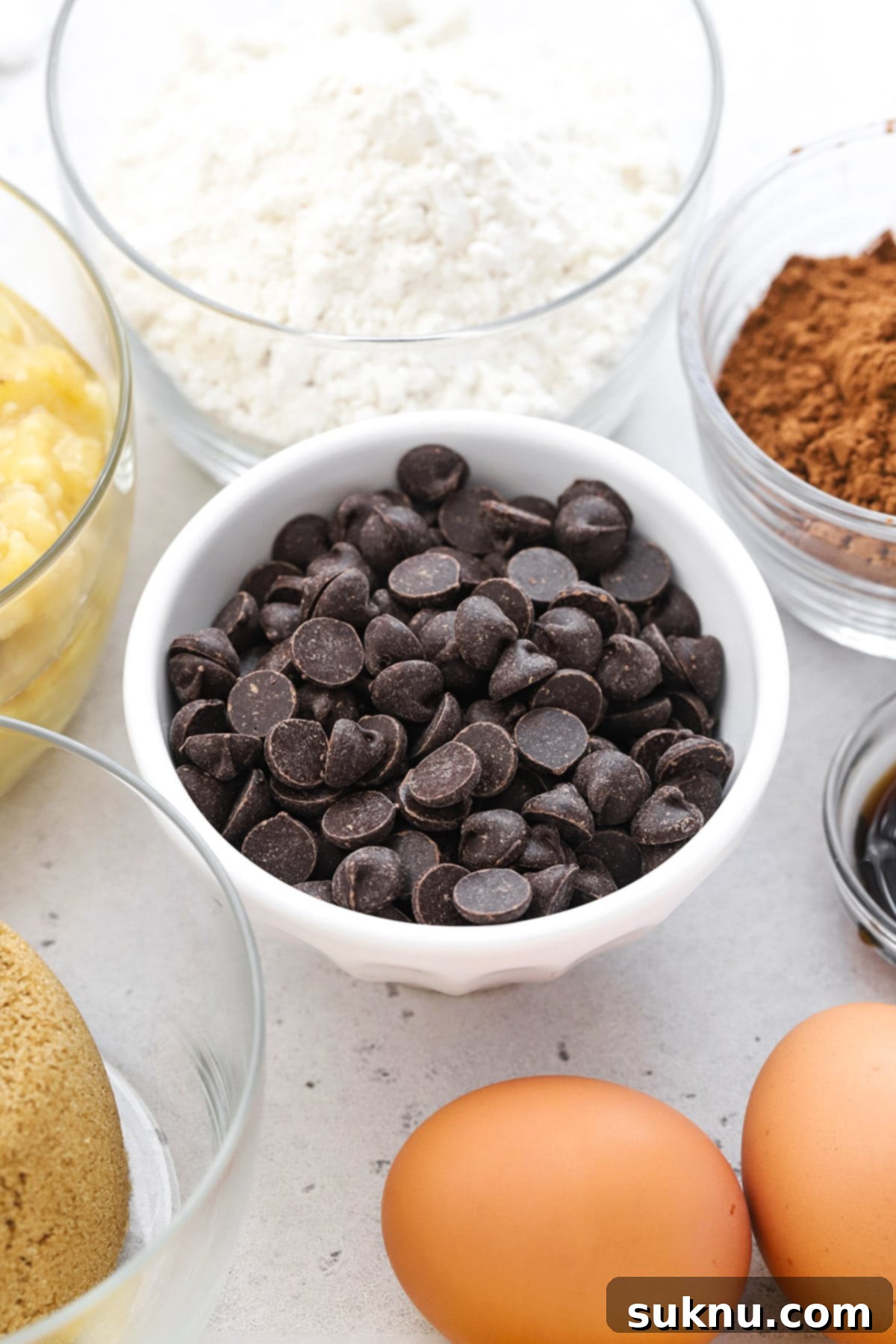Decadent Gluten-Free Chocolate Banana Bread 3 Front view of all the simple, high-quality ingredients laid out for making gluten-free chocolate banana bread: deeply spotted overripe bananas, melted golden butter, rich brown sugar, fresh eggs, vanilla extract, a cup of gluten-free flour blend, unsweetened cocoa powder, baking soda, a pinch of salt, and generous chocolate chips.