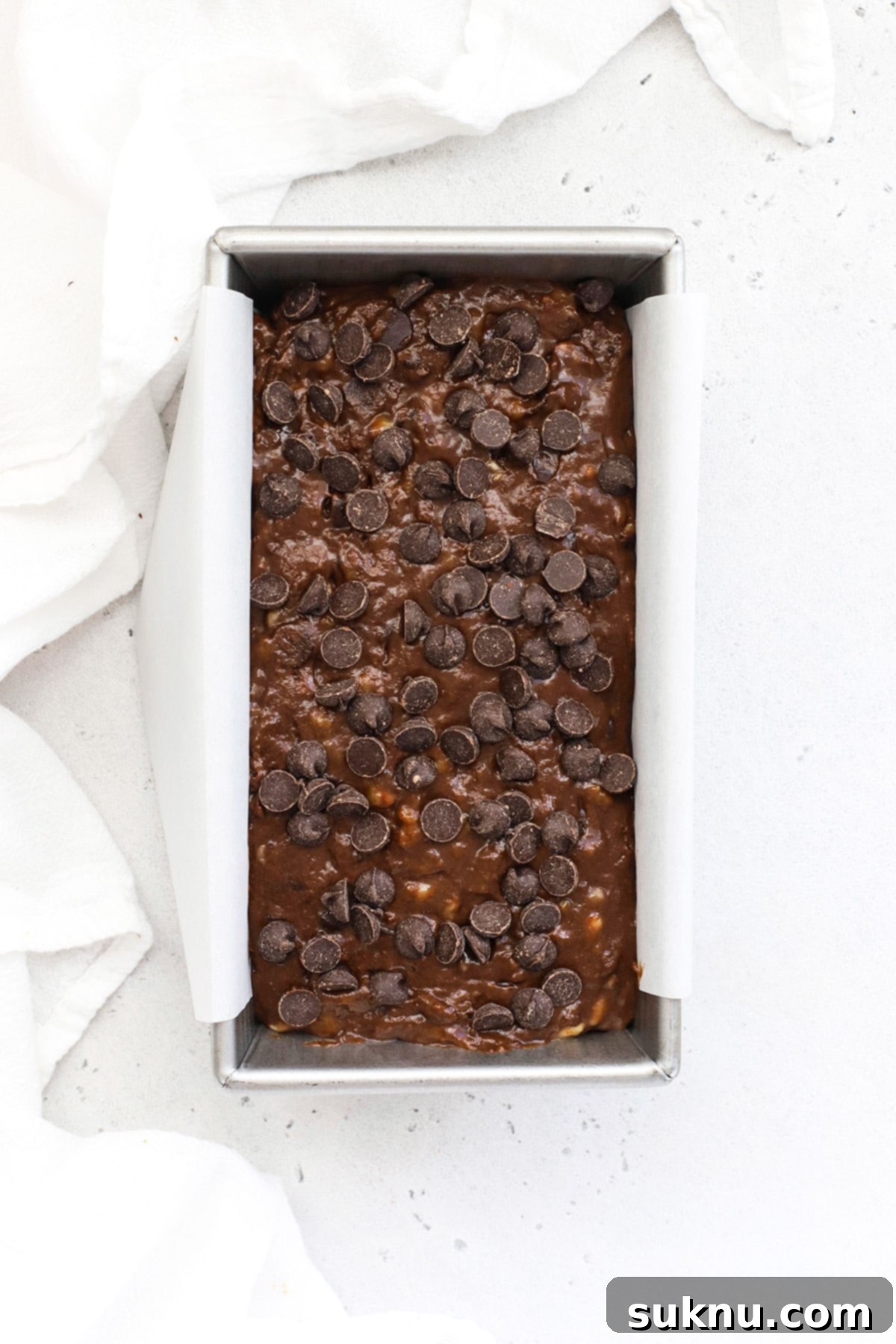 Decadent Gluten-Free Chocolate Banana Bread 9 An inviting overhead view of the unbaked gluten-free double chocolate banana bread, nestled in its parchment-lined loaf pan, with a perfect scattering of additional chocolate chips on its surface, ready for the oven.