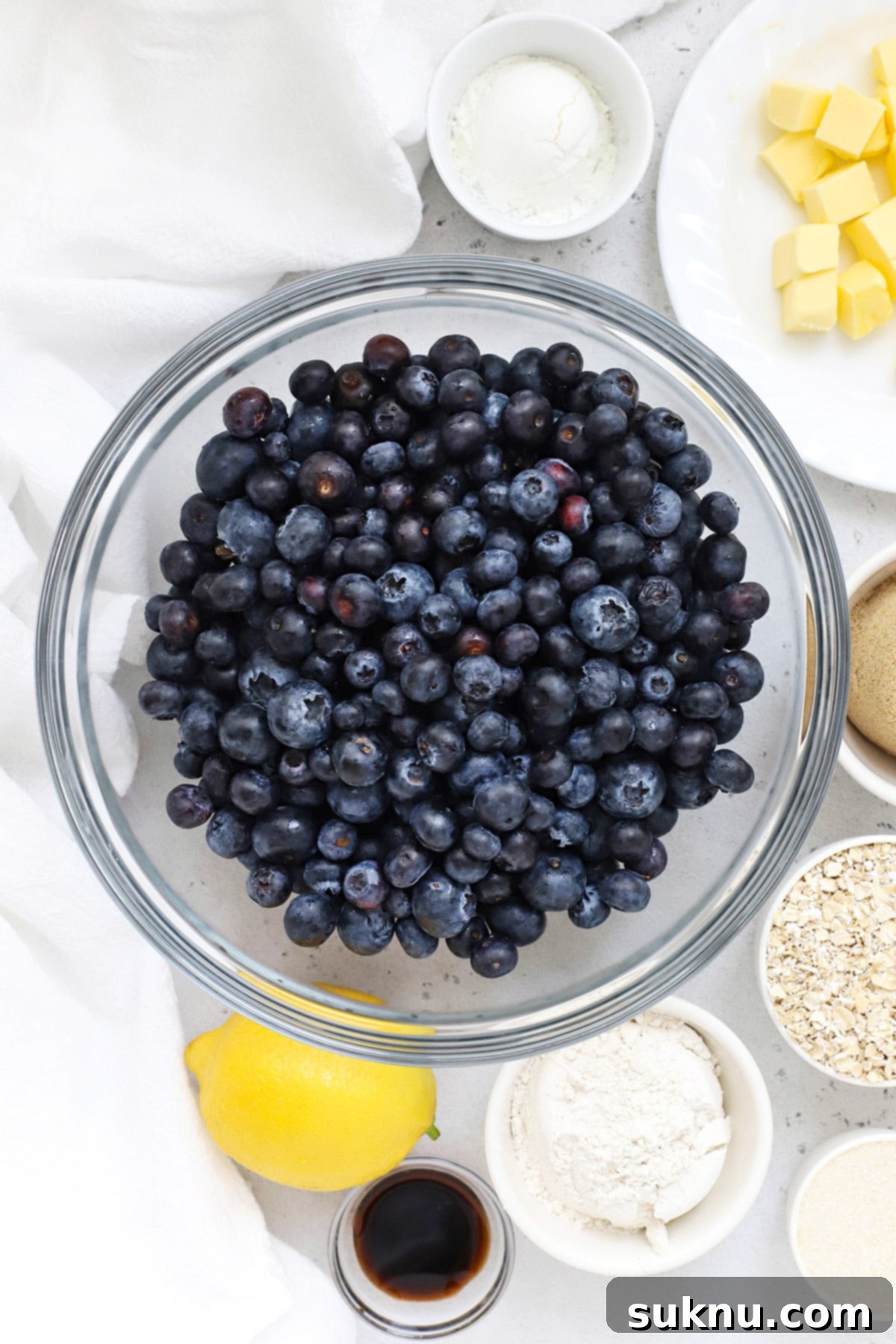 A selection of fresh ingredients laid out, including blueberries, lemons, sugar, butter, and gluten-free oats, ready for making blueberry crisp.