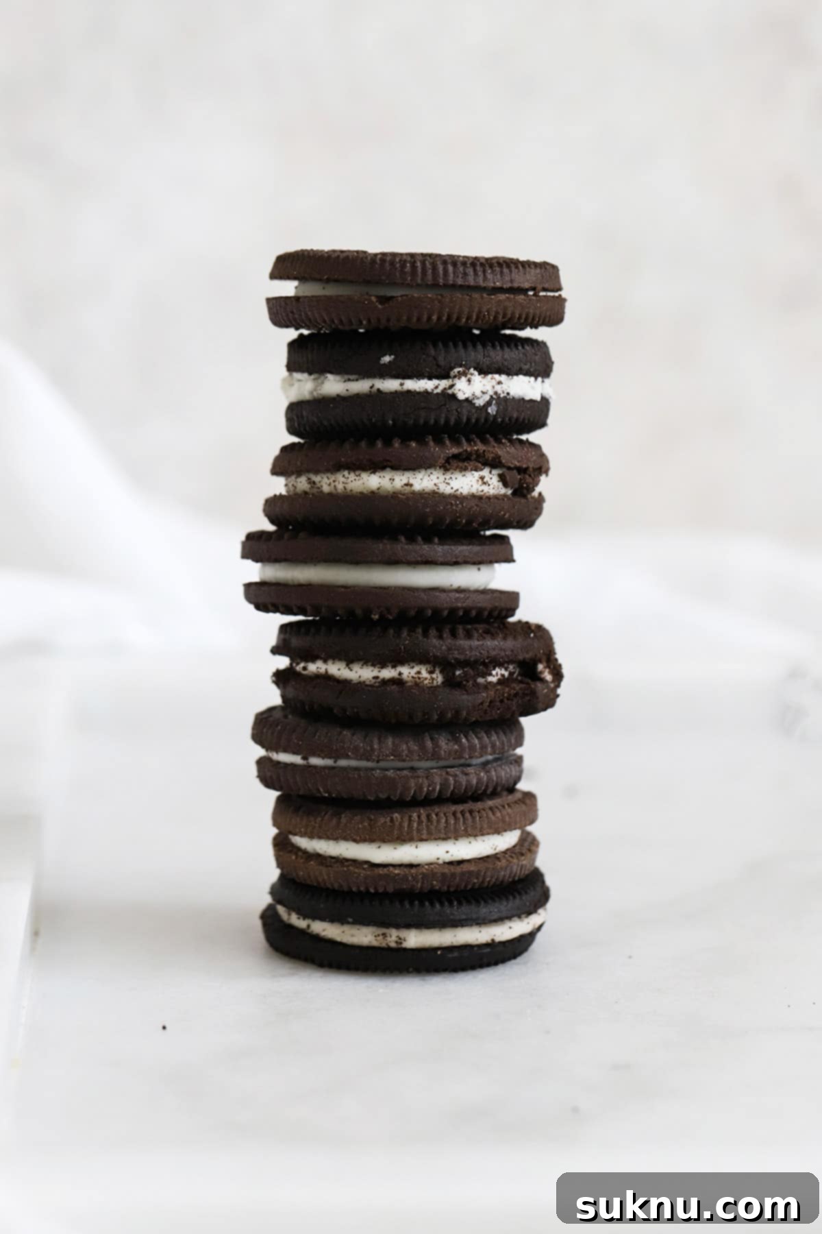 A stack of 8 different brands of gluten-free chocolate sandwich cookies, showcasing various packaging and cookie designs.