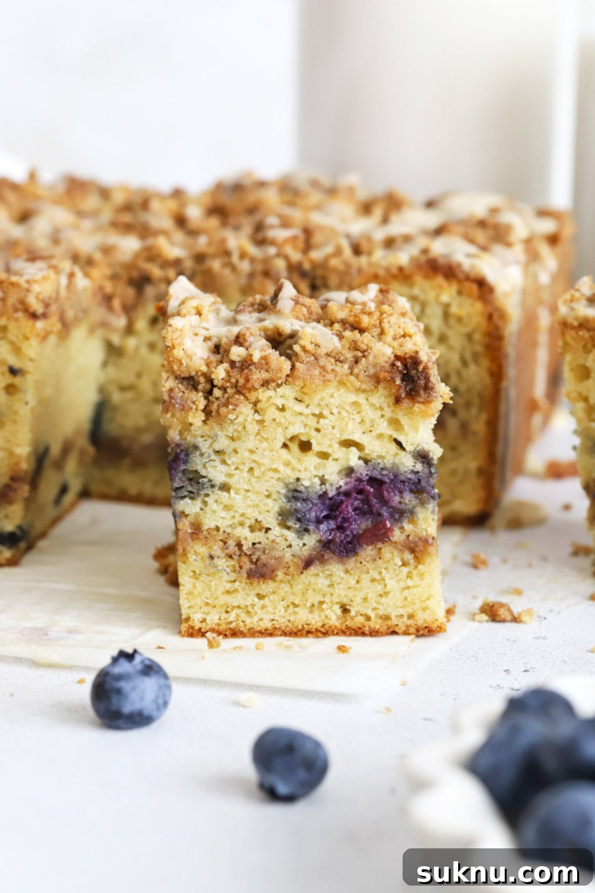 Front view of a slice of gluten-free blueberry coffee cake with cinnamon streusel & glaze