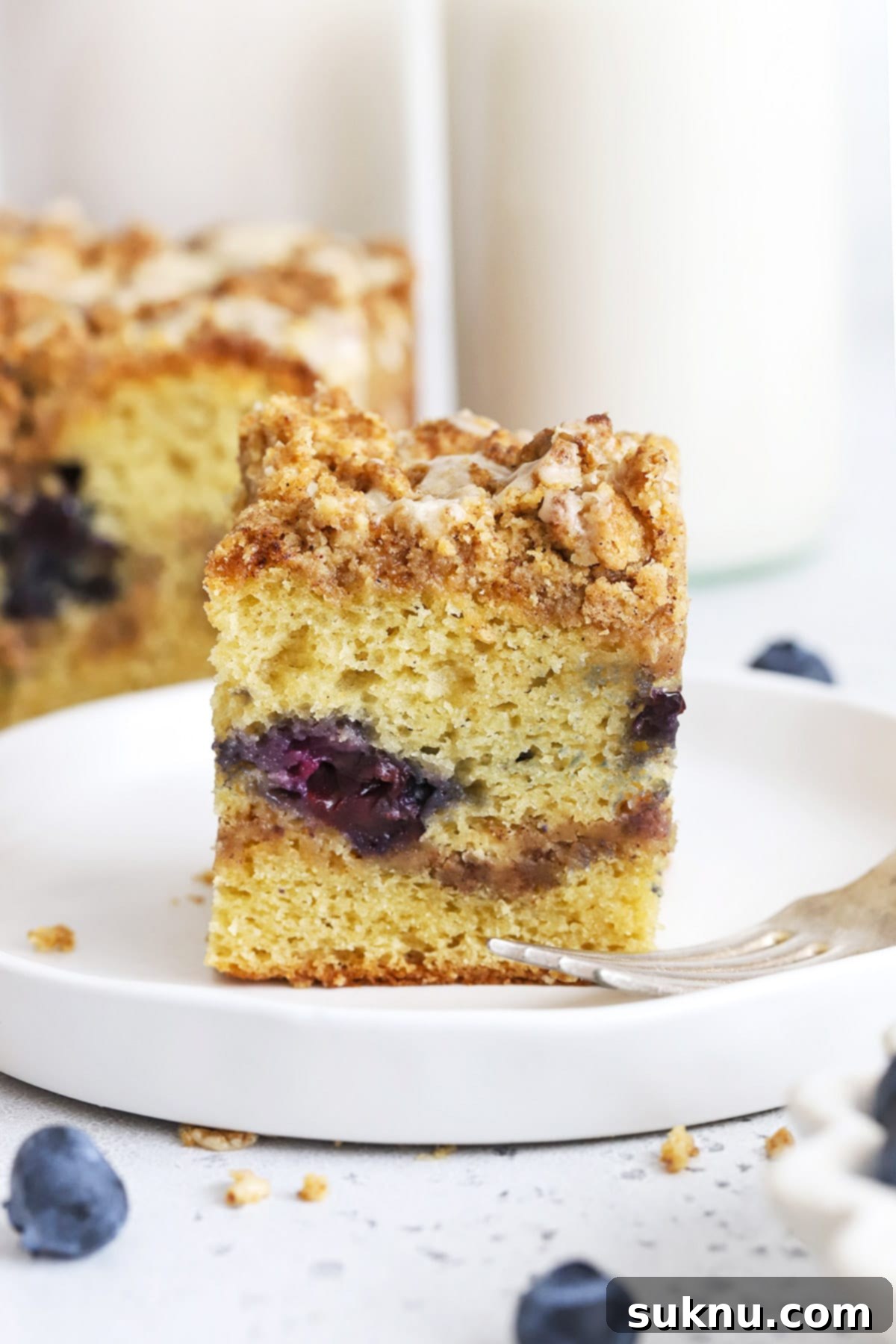 Front view of a slice of gluten-free blueberry coffee cake with cinnamon streusel & glaze
