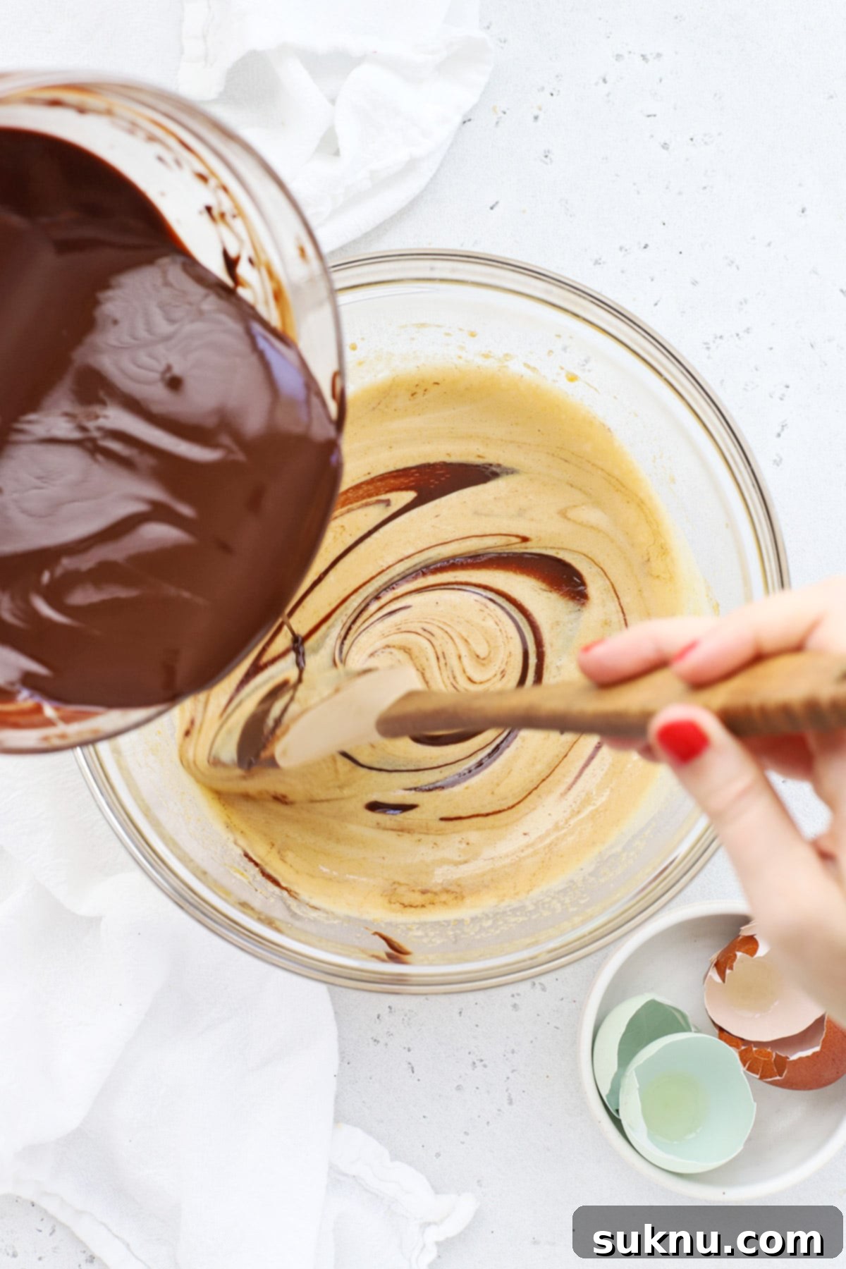 Adding melted chocolate to the aerated egg and sugar mixture for gluten-free brownie cookies batter.