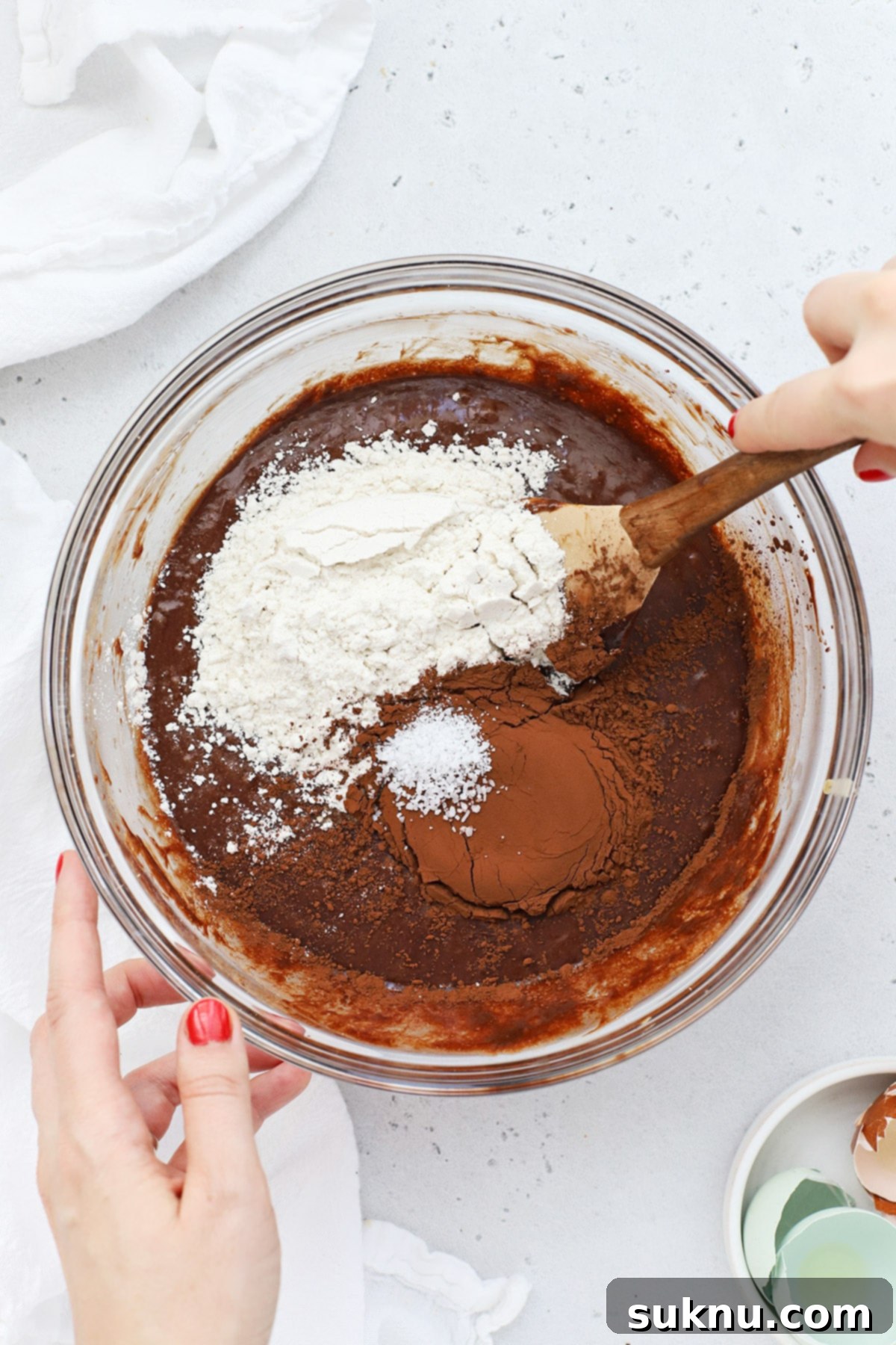 Adding dry ingredients (gluten-free flour, cocoa powder, salt) to the wet brownie cookie batter.