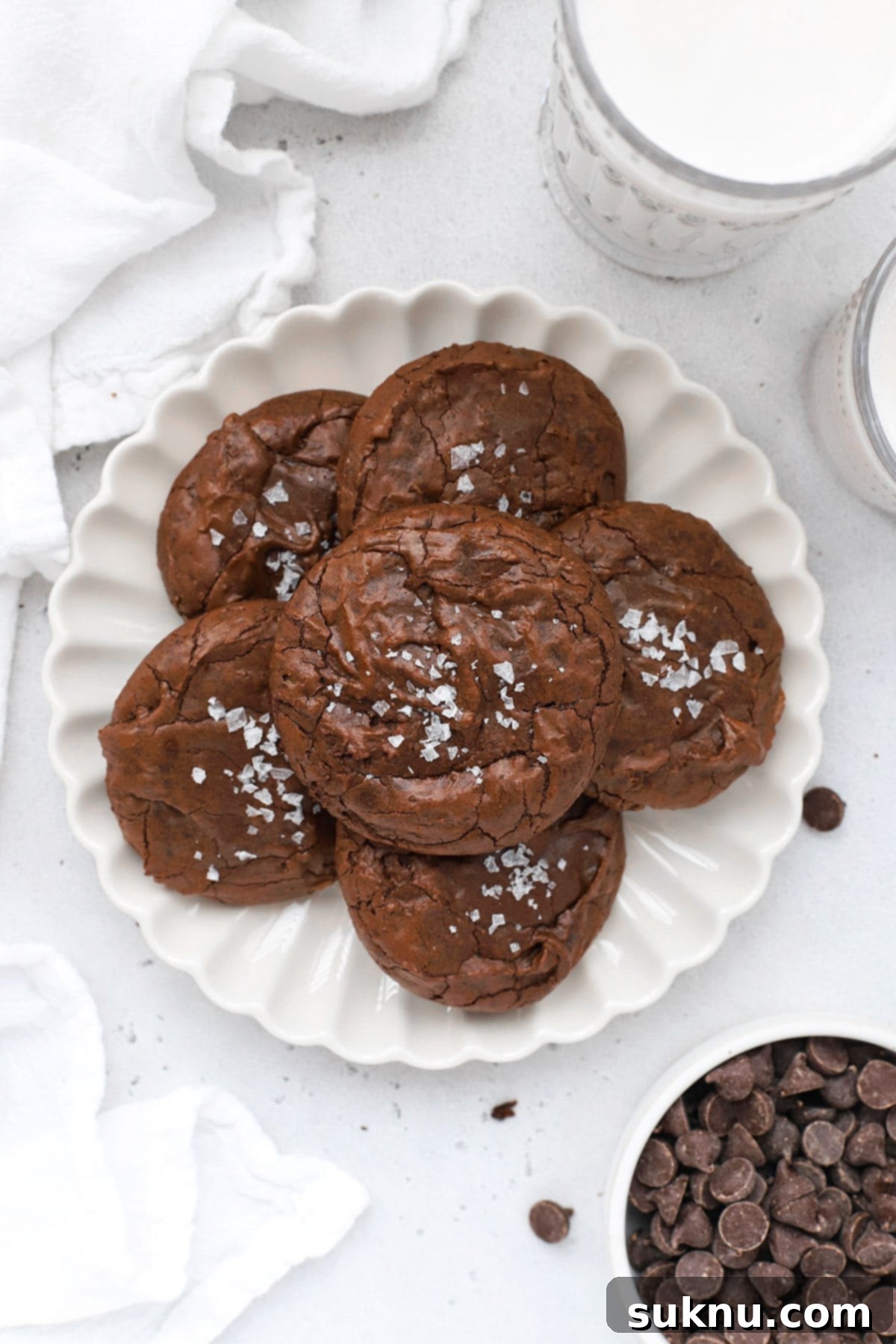 Overhead view of several gluten-free chocolate brownie cookies arranged on a ruffled white plate.