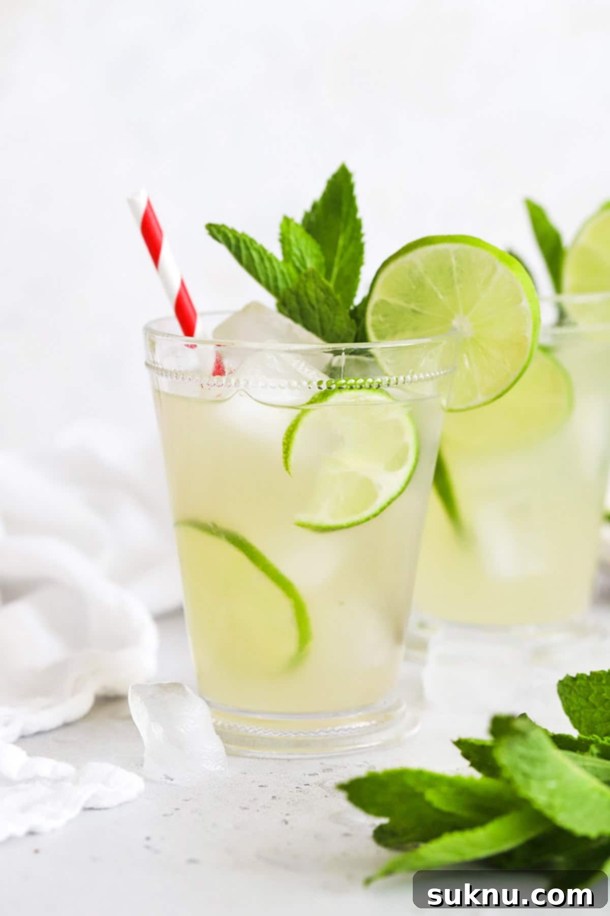 Zesty Mint Lime Mocktail 11 Two clear glasses of Virgin Mojito Mint Limeade, garnished with fresh mint and lime, sitting on a wooden surface.