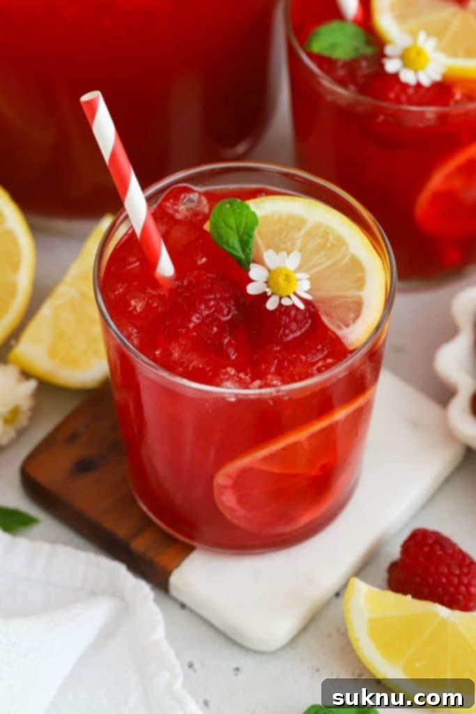 Zesty Mint Lime Mocktail 13 A tall glass of bright pink raspberry lemonade, garnished with fresh raspberries and a lemon slice.