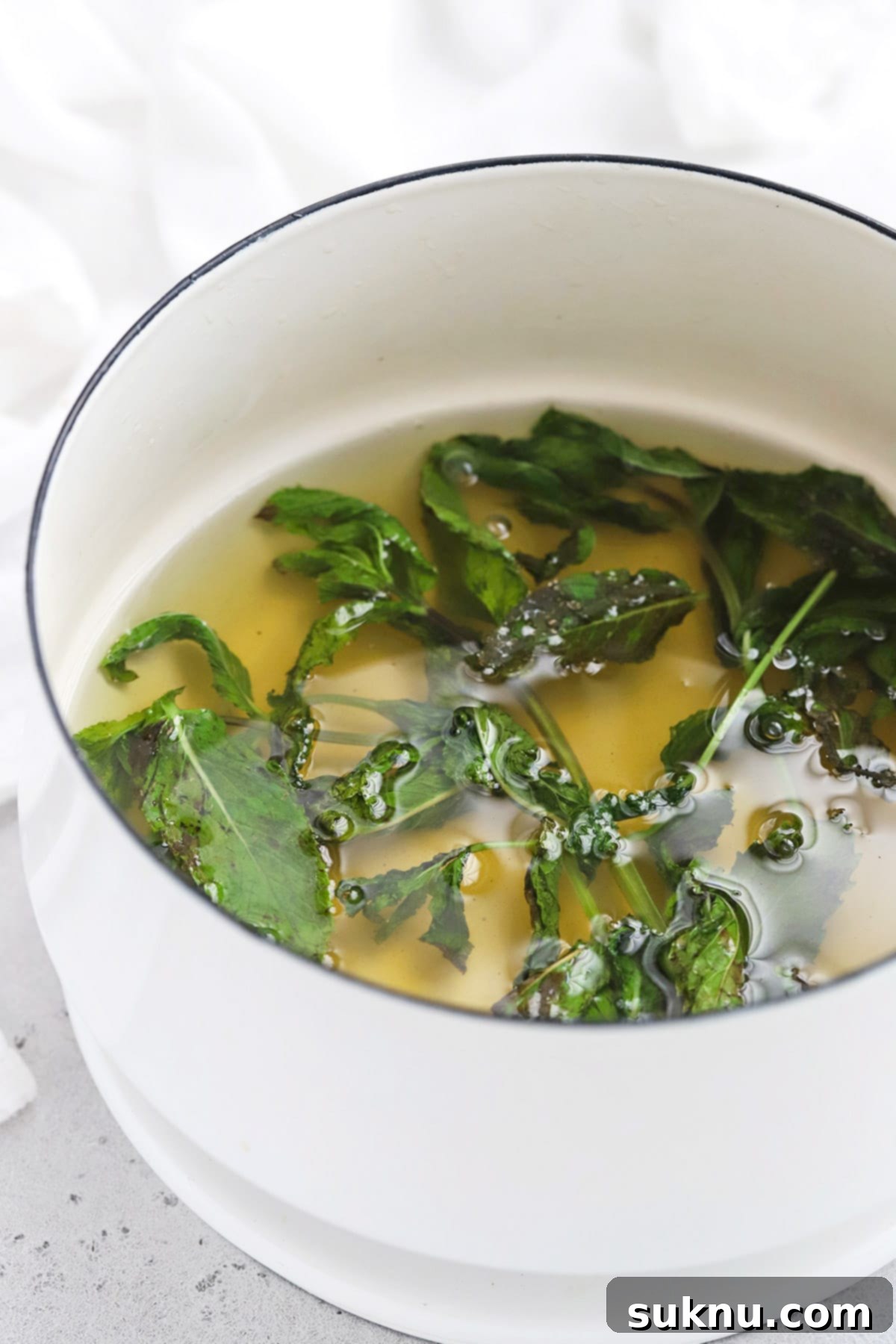 Zesty Mint Lime Mocktail 5 Mint leaves steeping in hot simple syrup in a saucepan, infusing their fresh flavor.