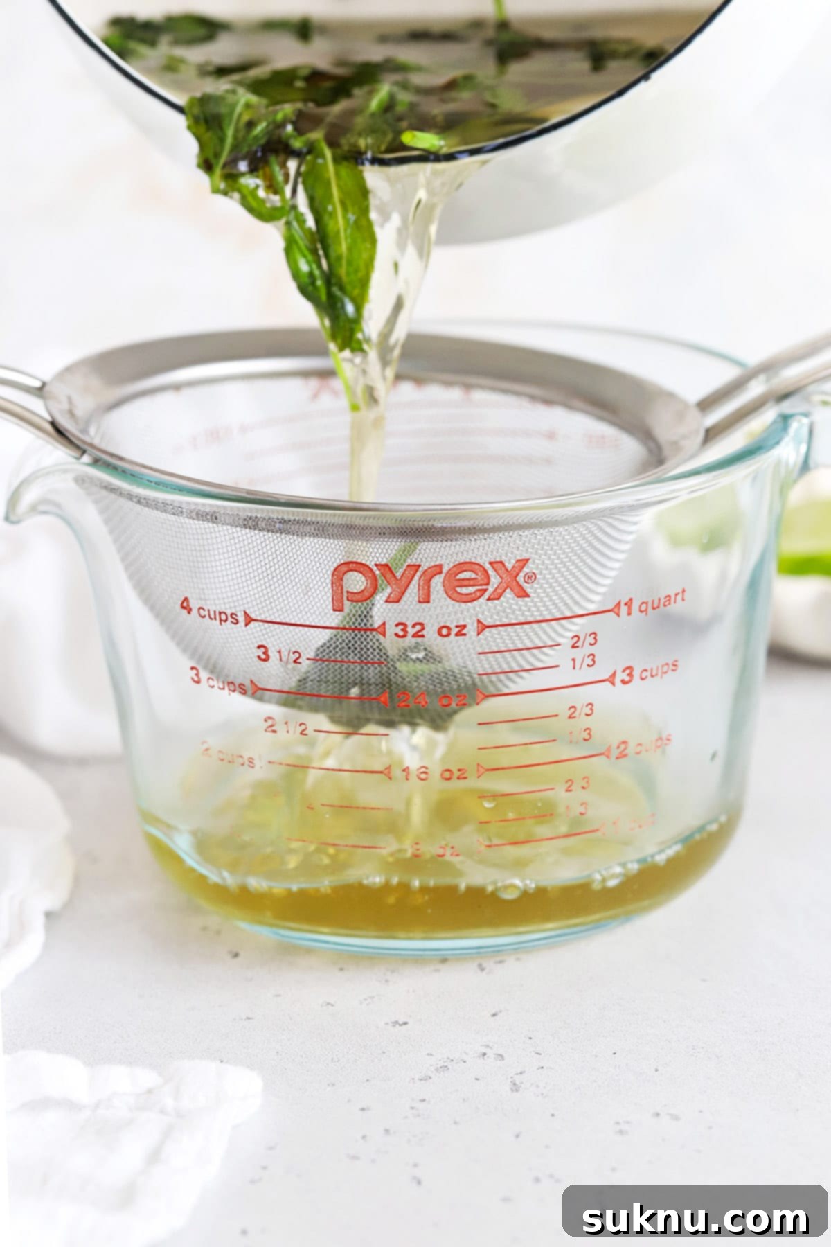 Zesty Mint Lime Mocktail 7 A fine mesh sieve being used to strain mint leaves from simple syrup into a glass measuring cup.