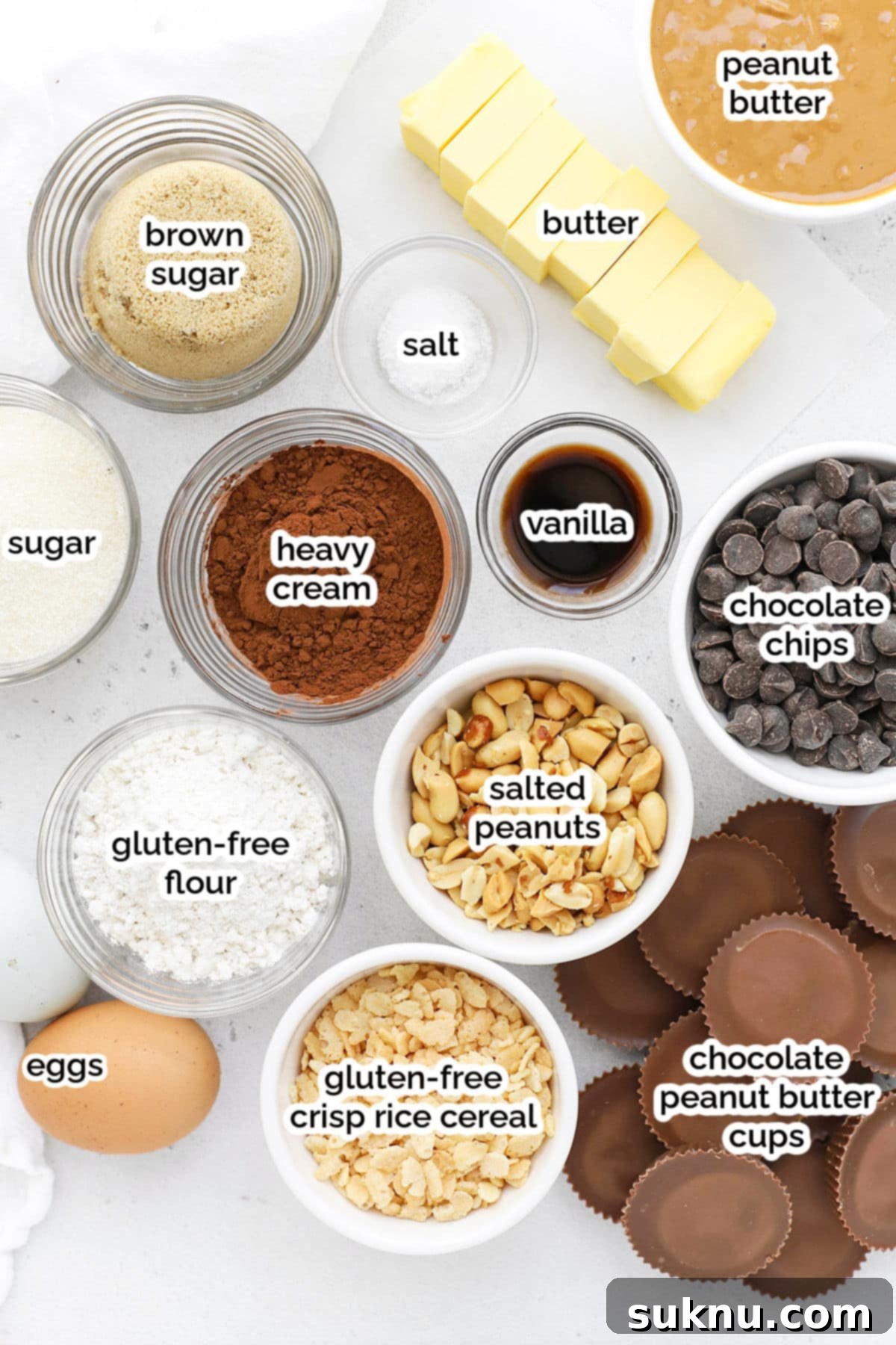 Collection of ingredients laid out for making gluten-free peanut butter cup brownies, including butter, sugar, eggs, flour, cocoa, peanut butter cups, and crisp rice cereal.