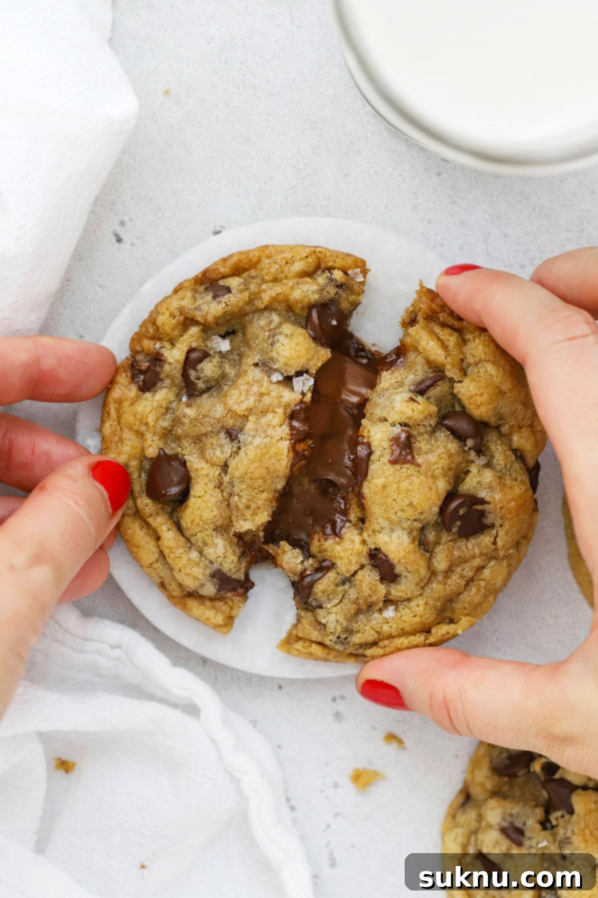 Pulling apart a gluten-free Nutella chocolate chip cookie, revealing its gooey Nutella center, highlighting the rich texture and delicious filling.