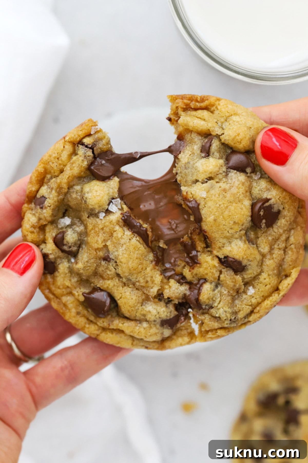 A close-up shot of a gluten-free Nutella chocolate chip cookie being pulled apart, showcasing the incredibly gooey, melted Nutella filling.