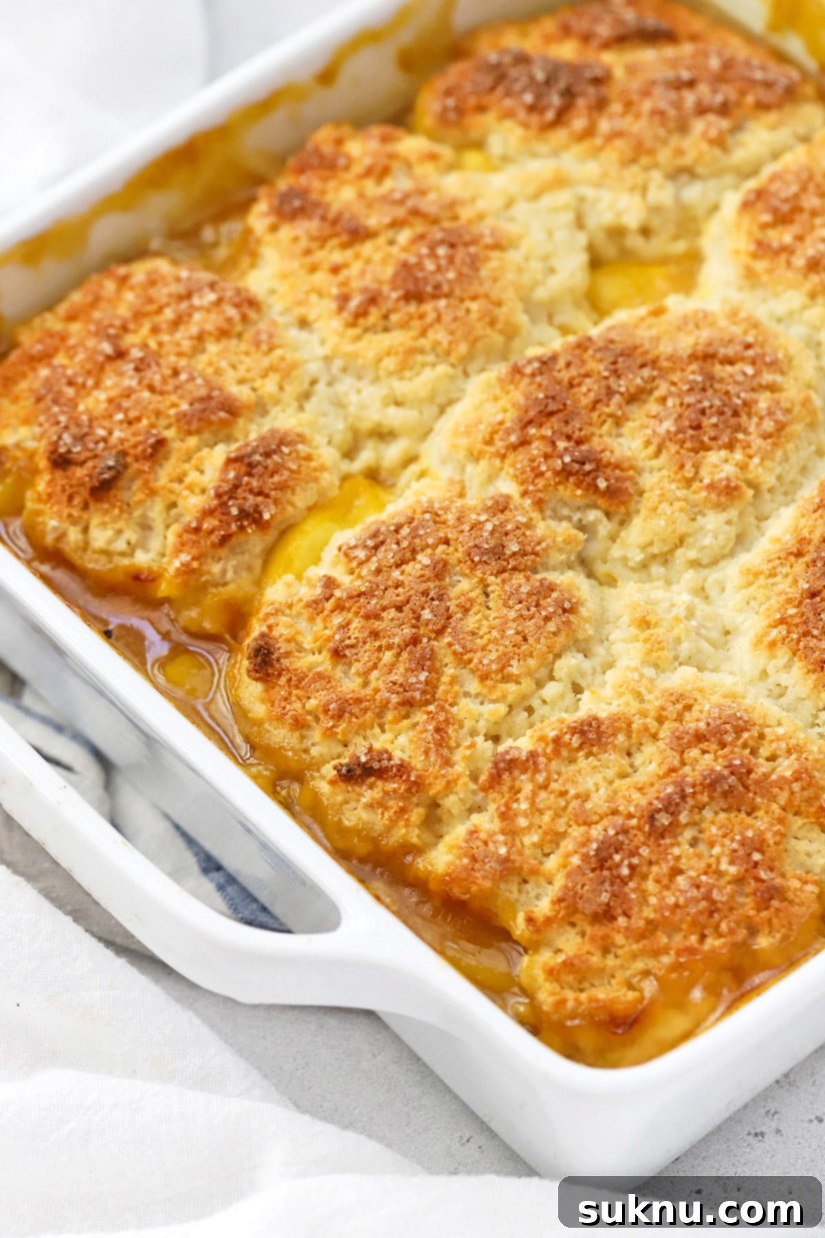 Simple Delicious Gluten-Free Peach Cobbler 11 Close-up shot of a freshly baked gluten-free peach cobbler, showcasing the perfectly golden-brown, sweet biscuit topping and the vibrant, bubbling peach filling beneath.