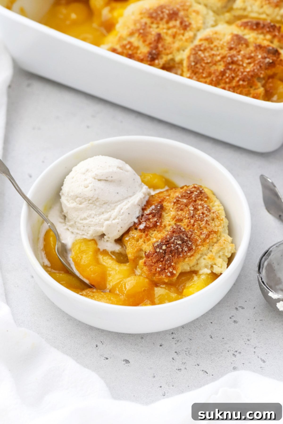 Simple Delicious Gluten-Free Peach Cobbler 12 A beautiful, warm gluten-free peach cobbler served in a bowl, generously topped with a dollop of melting vanilla ice cream, perfectly arranged for a delicious bite.