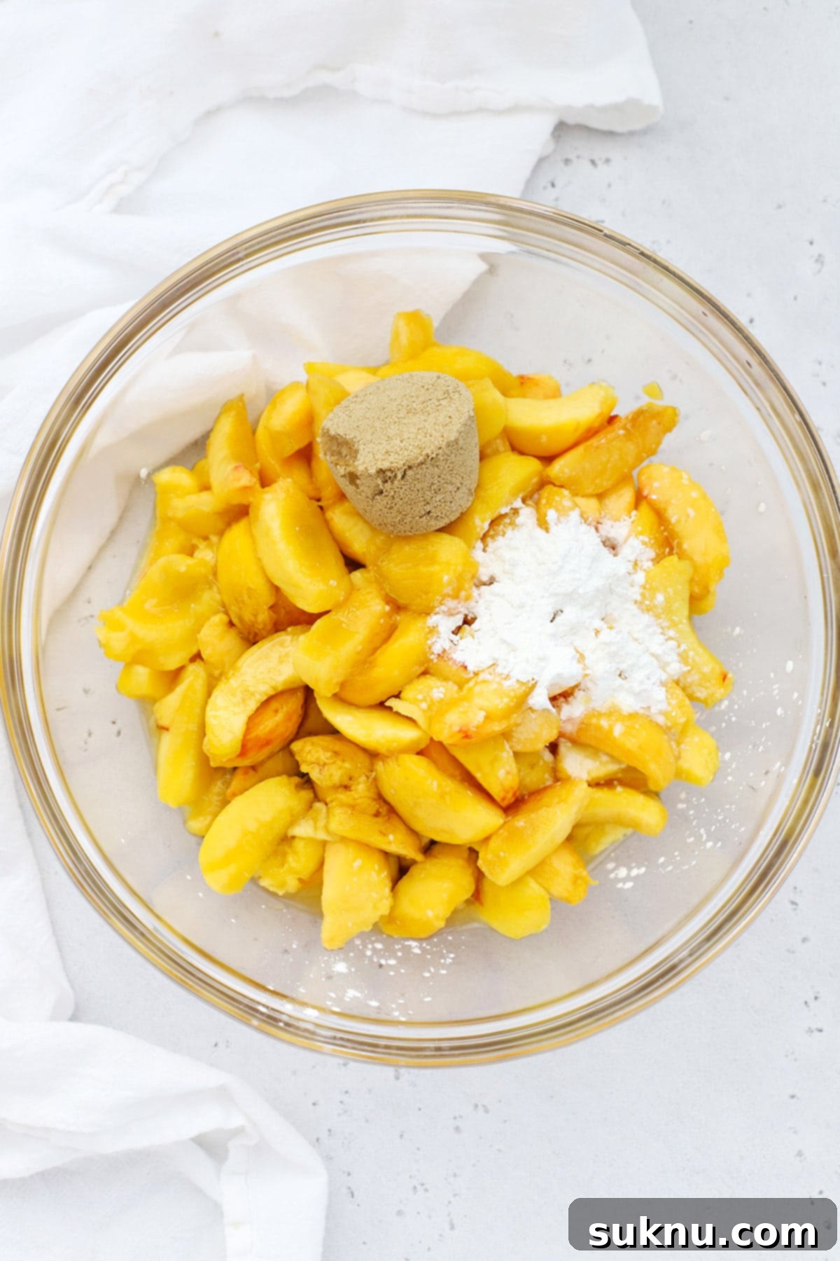 Simple Delicious Gluten-Free Peach Cobbler 4 Overhead view of all the fresh ingredients for gluten-free peach cobbler filling, including sliced peaches, brown sugar, and extracts, neatly arranged in a bowl.