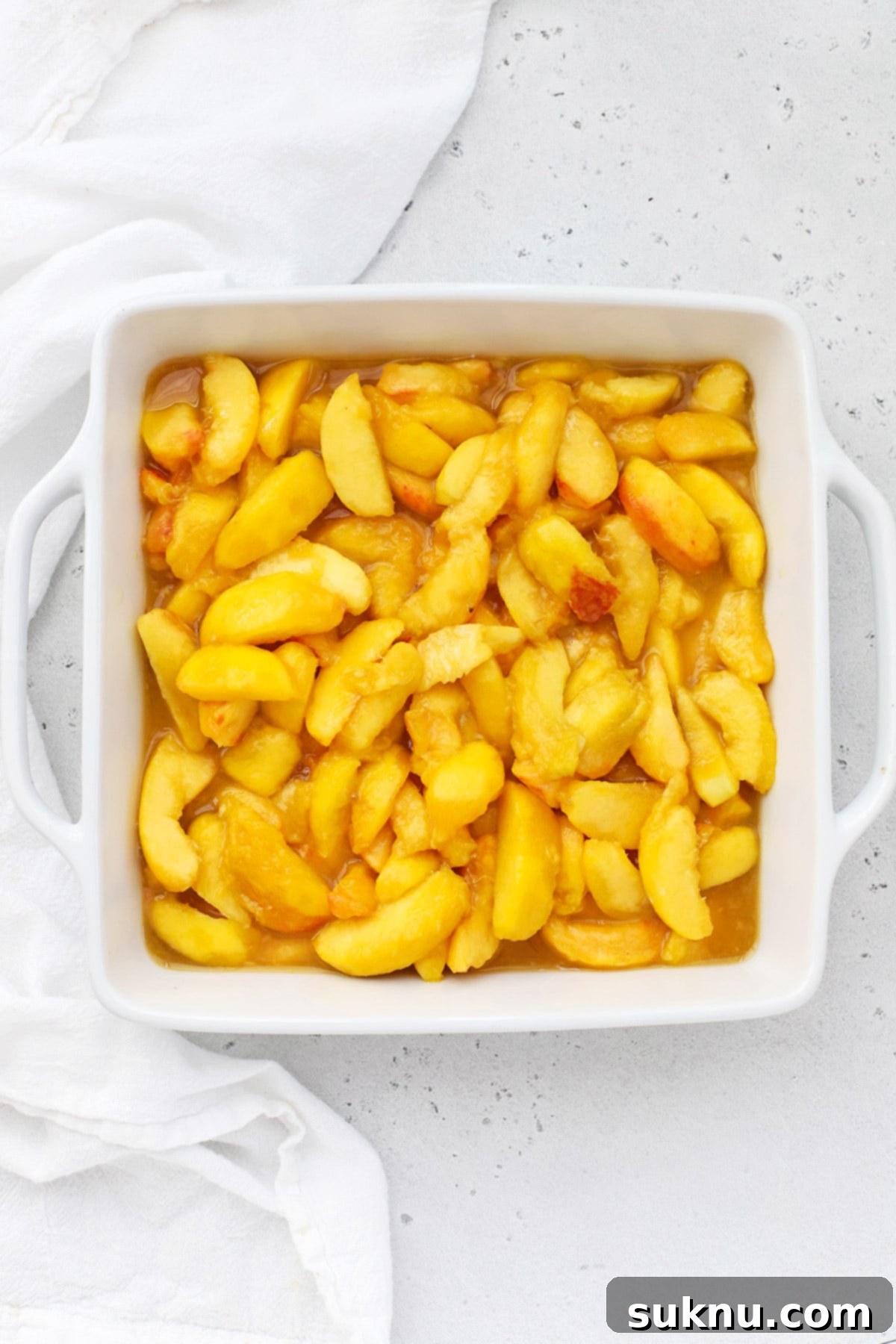 Simple Delicious Gluten-Free Peach Cobbler 5 Close-up overhead shot of the vibrant gluten-free peach filling, glistening and evenly spread in a clear glass baking dish, ready for its topping.