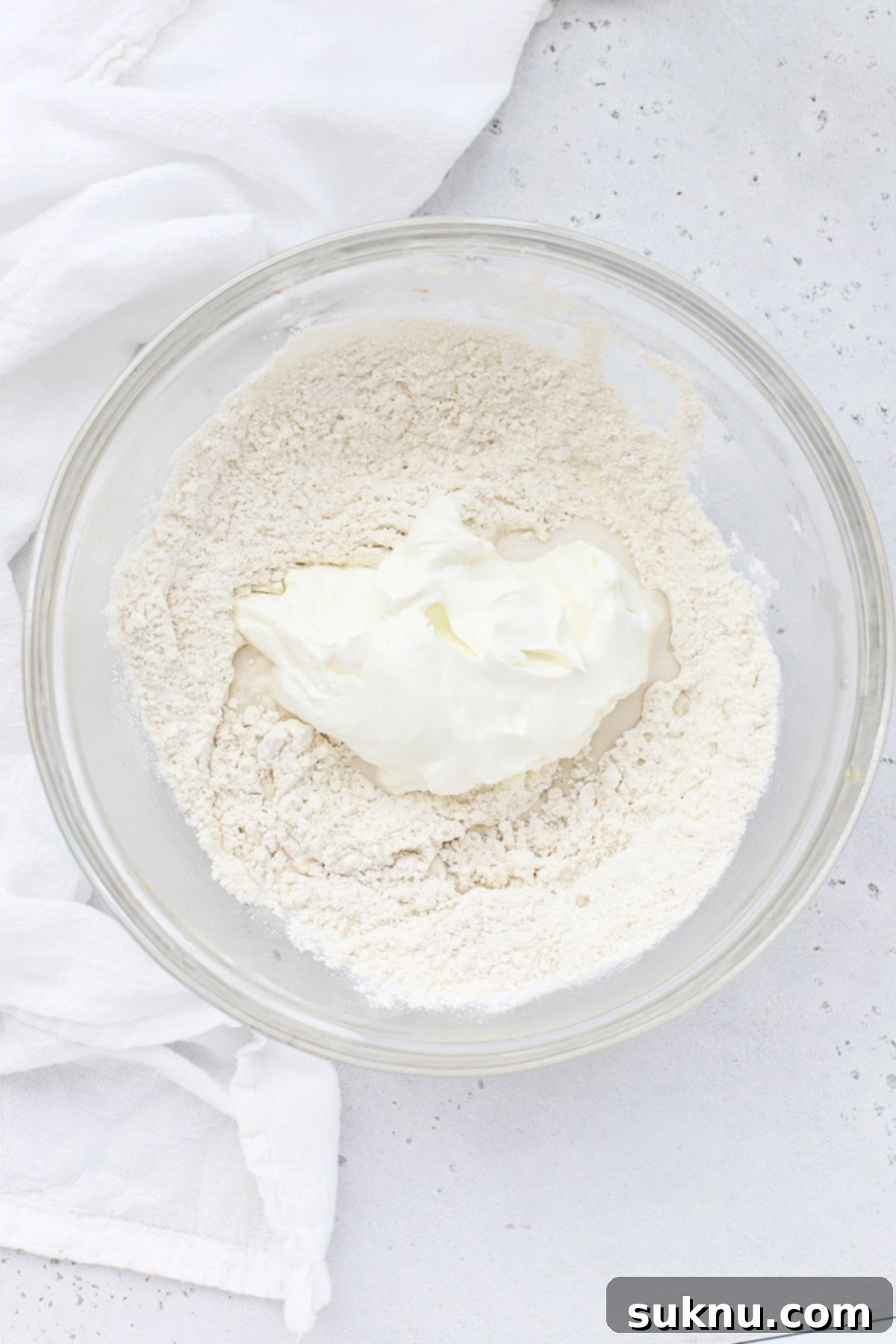 Simple Delicious Gluten-Free Peach Cobbler 6 Hands carefully adding creamy Greek yogurt to the dry ingredients for the gluten-free biscuit topping, a crucial step for achieving tender biscuits.