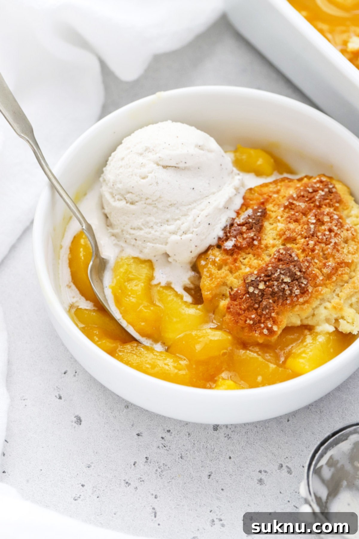 Simple Delicious Gluten-Free Peach Cobbler 10 A close-up shot of a bowl filled with easy gluten-free peach cobbler, generously topped with a scoop of melting vanilla ice cream, creating a delightful contrast of temperatures and textures.