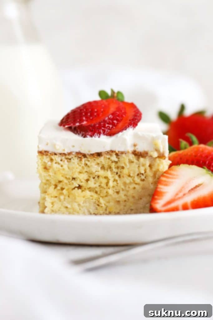 A slice of gluten-free tres leches cake topped with fresh strawberries on a white plate