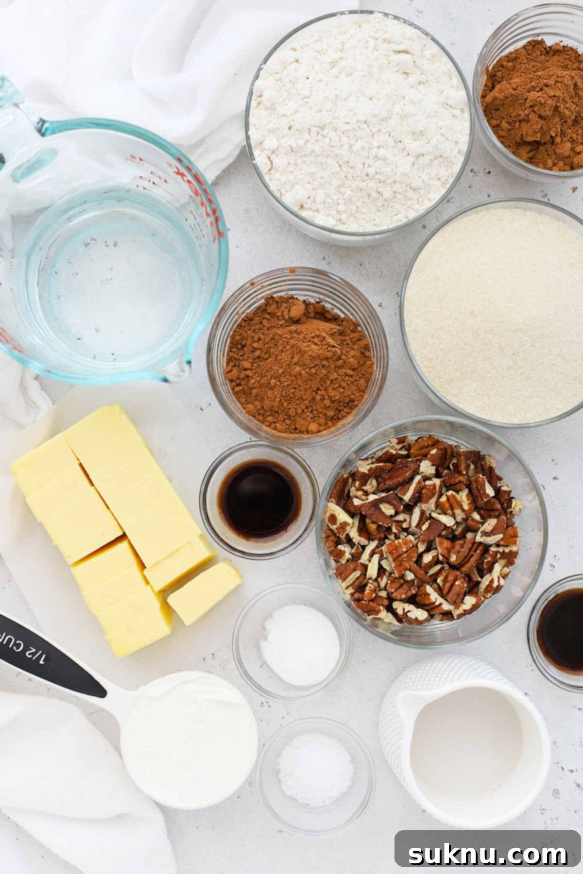 A flat lay photograph showcasing all the simple ingredients required for making gluten-free Texas sheet cake, including flour, sugar, cocoa, butter, eggs, and sour cream.