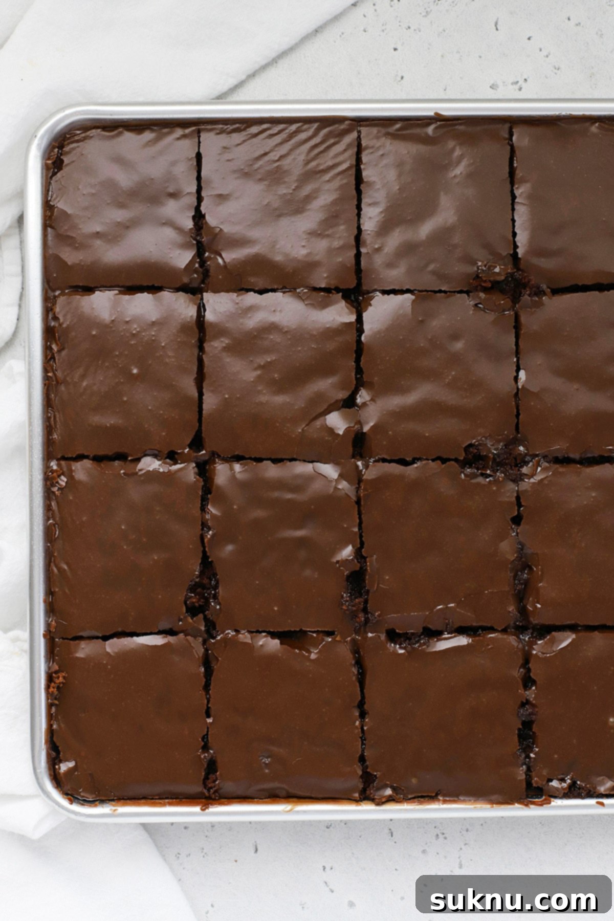 A freshly baked gluten-free Texas chocolate sheet cake, cut into neat squares and ready to be served, highlighting its moist texture and shiny fudge frosting.