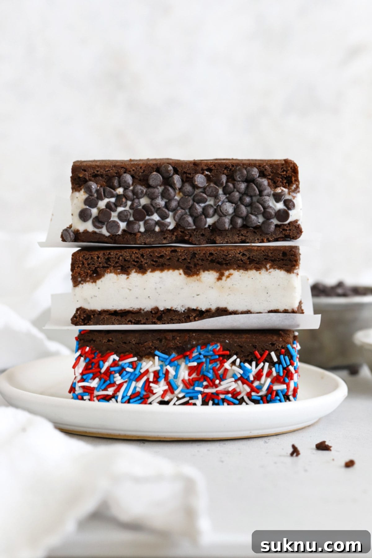 Three gluten-free brownie ice cream sandwiches on a plate. One is rolled in chocolate chip and one is rolled in red, white, and blue sprinkles