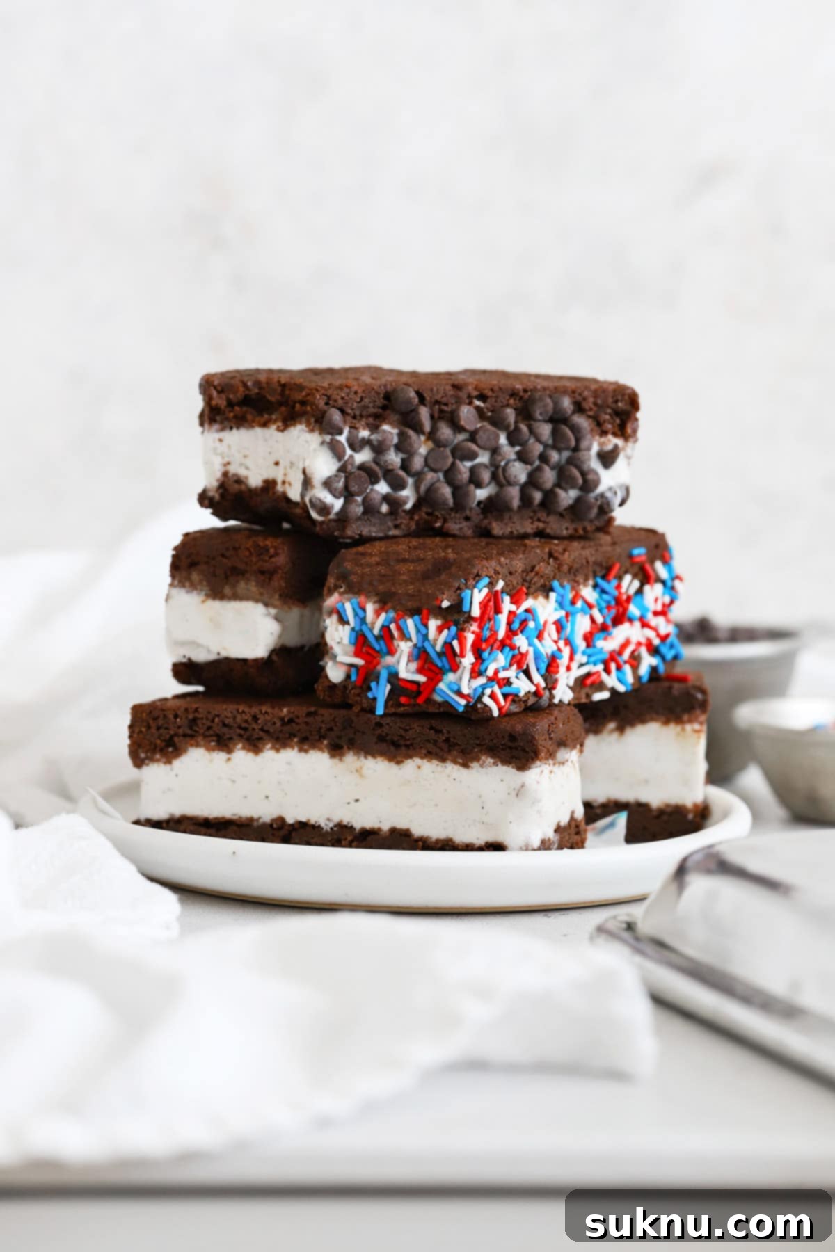 Gluten free ice cream sandwiches stacked on a plate. One is rolled in mini chocolate chips and one is rolled in red, white, and blue jimmies sprinkles