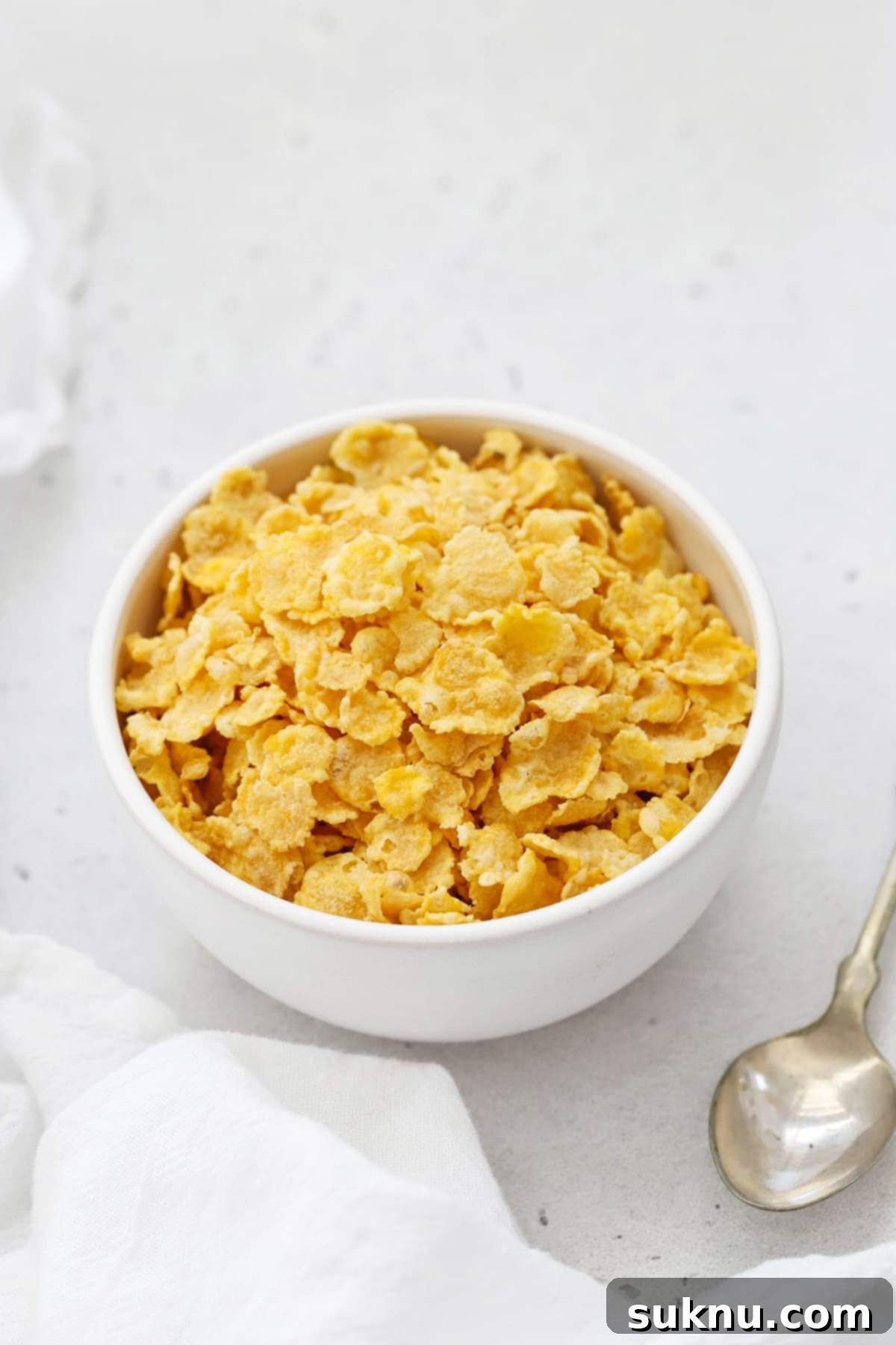 A close-up shot of crispy gluten-free corn flakes in a white bowl with milk