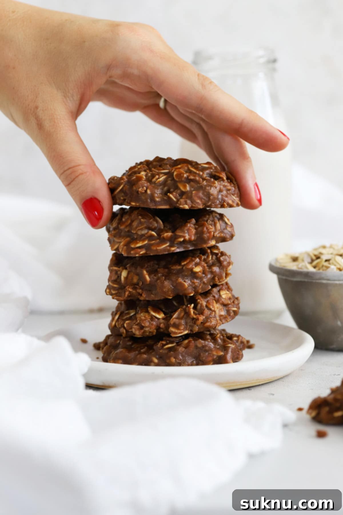 A stack of five gluten-free no-bake cookies on a white plate with a bottle of milk in the background