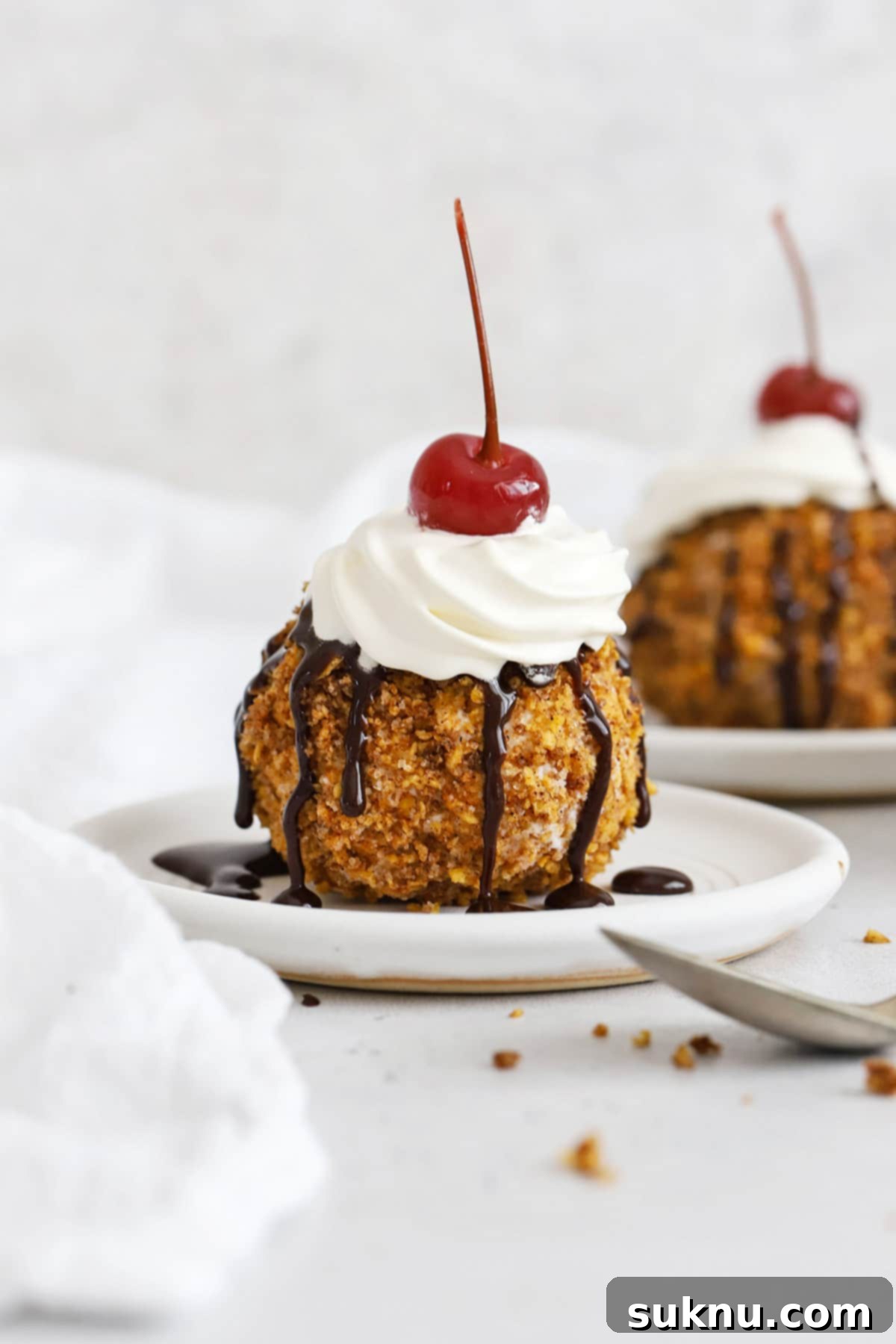 Front view of gluten-free fried ice cream topped with whipped cream, chocolate syrup, and a maraschino cherry