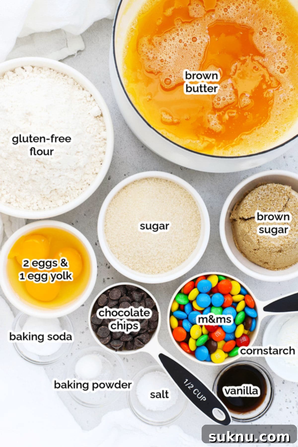 Soft & Chewy Gluten-Free M&M Cookies 3 A collection of ingredients for gluten-free M&M cookies, including flour, sugars, eggs, butter, M&Ms, and chocolate chips, laid out on a marble countertop