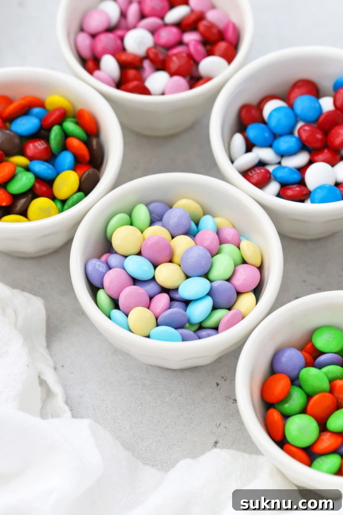 Which M&Ms Are Gluten-Free 7 Front view of small bowls of holiday m&m's--original, valentine's m&m's, red white and blue m&m's, Christmas red and green m&m's, orange green and purple Halloween m&m's and pastel Easter m&m's