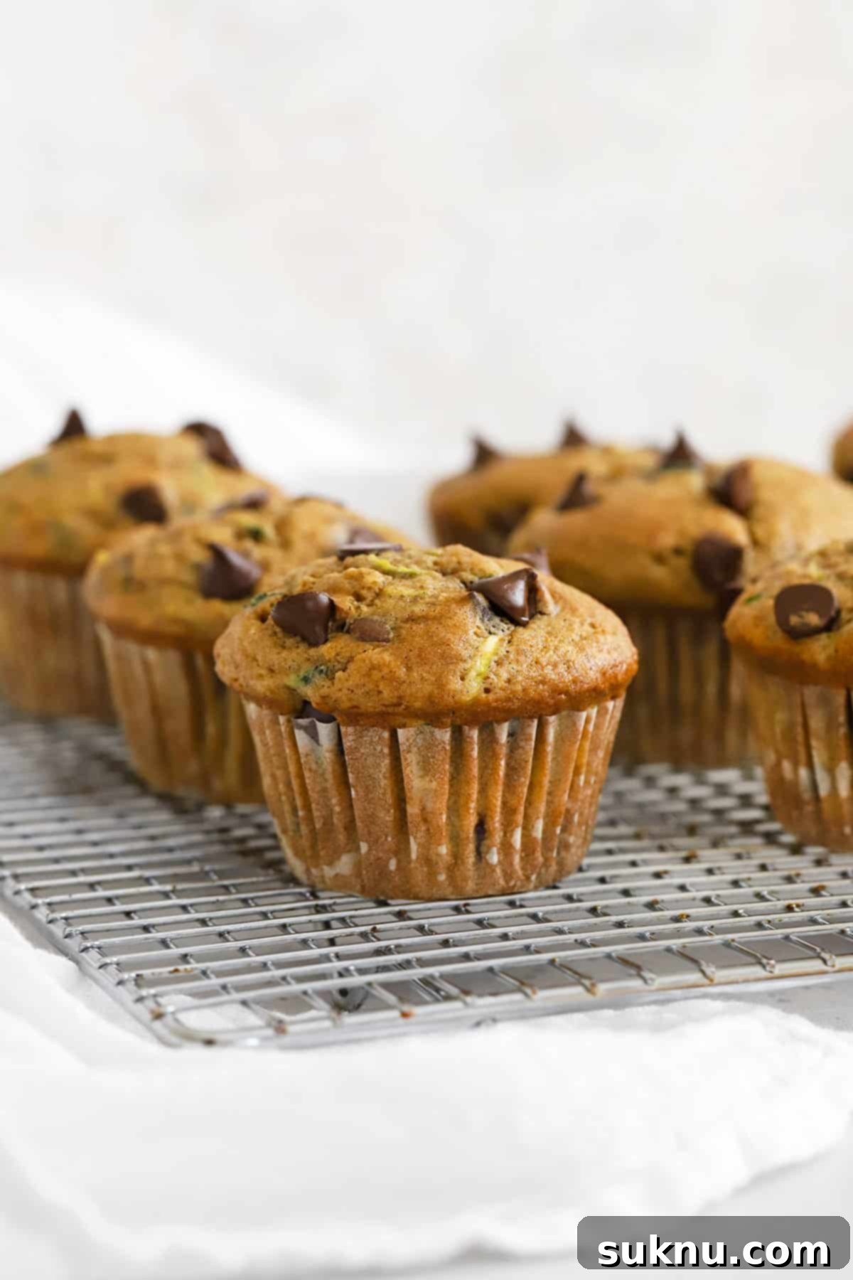 A front view of several gluten-free chocolate chip zucchini muffins cooling on a wire rack, showcasing their golden-brown tops and moist texture.
