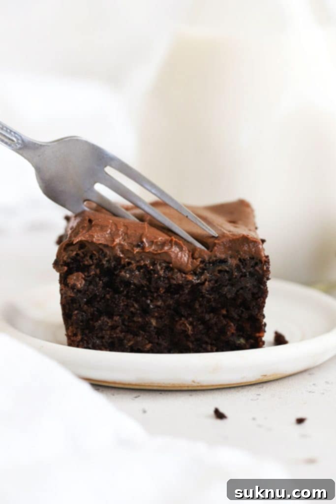 A fork cutting into a slice of decadent gluten-free chocolate zucchini cake topped with rich chocolate frosting.