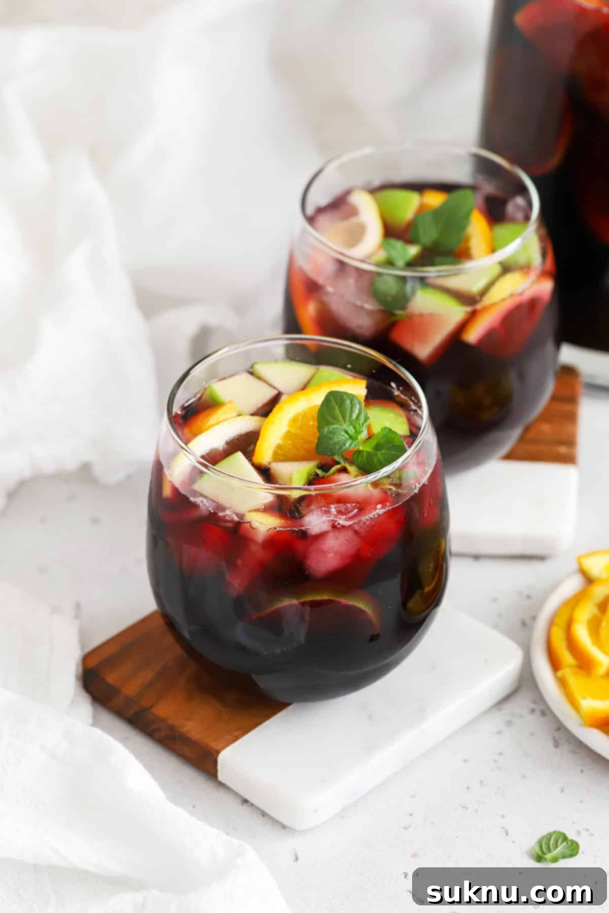Front view of two stemless glasses of non-alcoholic sangria, garnished with fresh fruit slices
