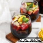 Front view of two stemless glasses of non-alcoholic sangria, garnished with fresh fruit slices