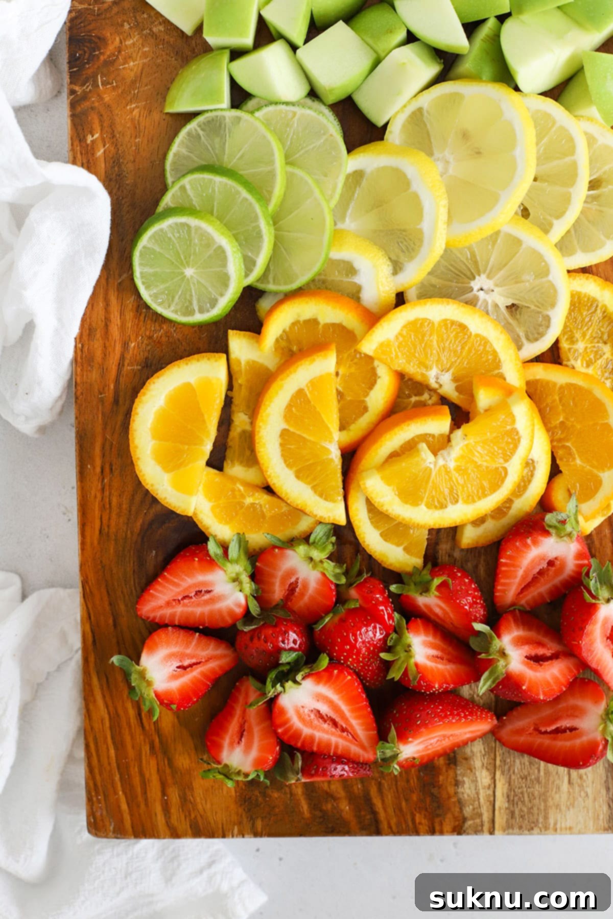 Overhead view of sliced and chopped fruit, including oranges, lemons, limes, green apples, and strawberries, ready for making virgin sangria