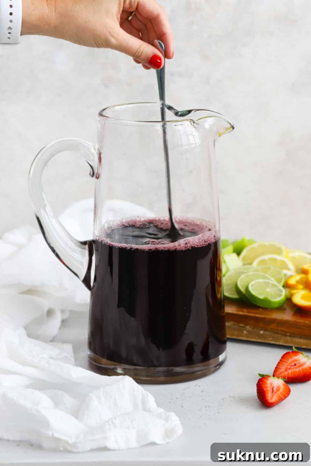 A person stirring grape and pomegranate juice in a large pitcher to make virgin sangria