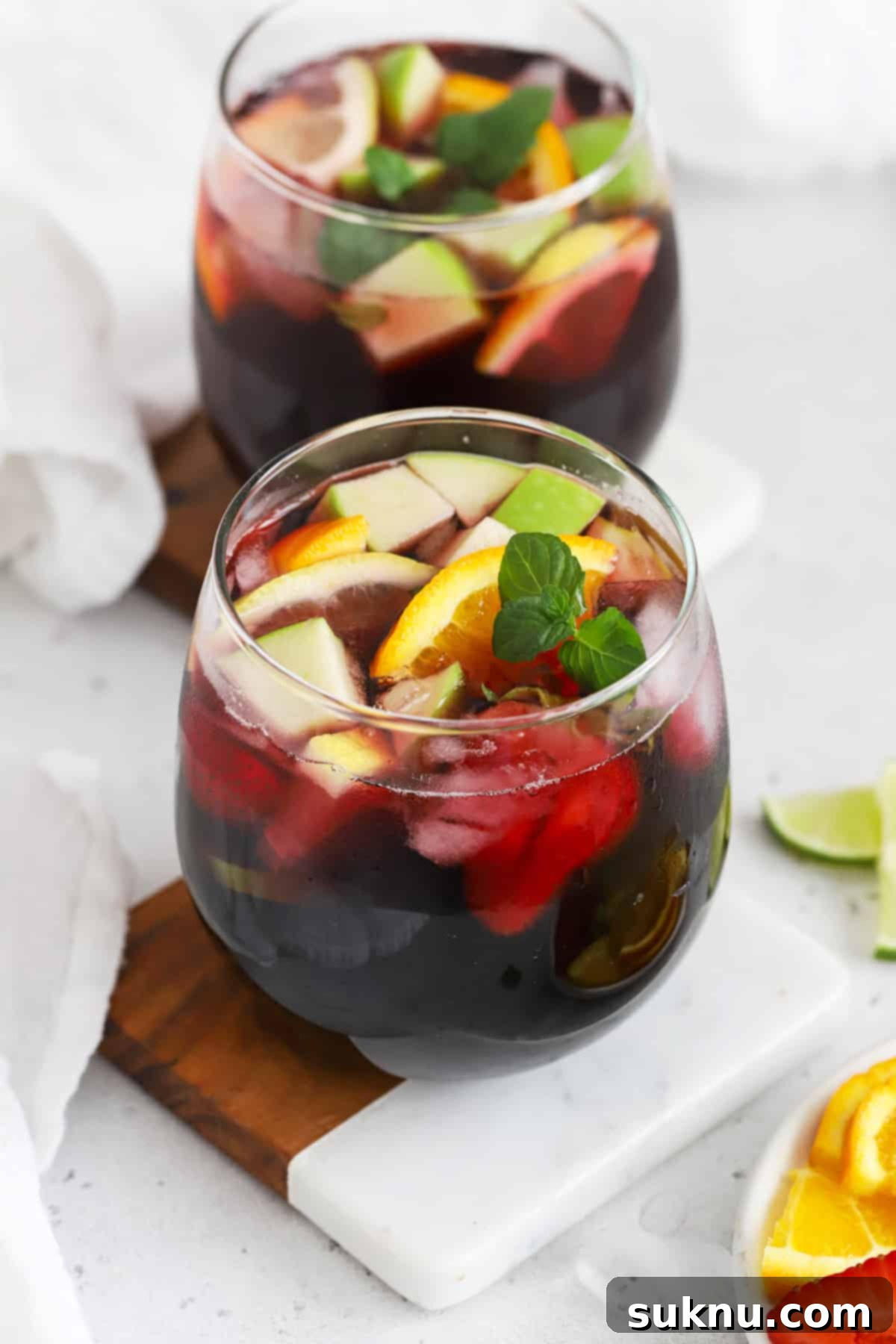 Front view of two stemless glasses filled with non-alcoholic sangria, showing the vibrant fruit and red liquid