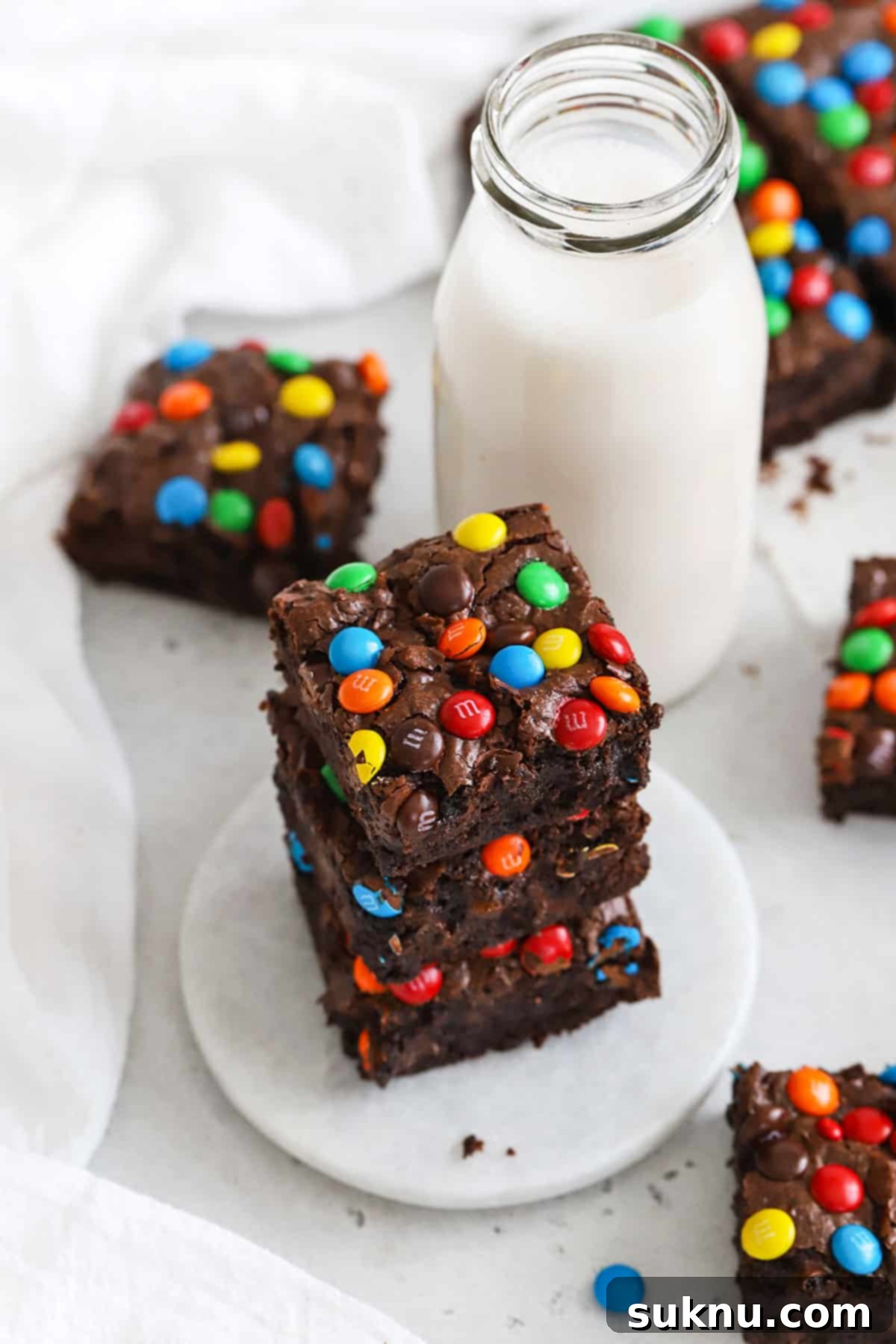 Chewy gluten-free M&M Brownies stacked next to a bottle of milk