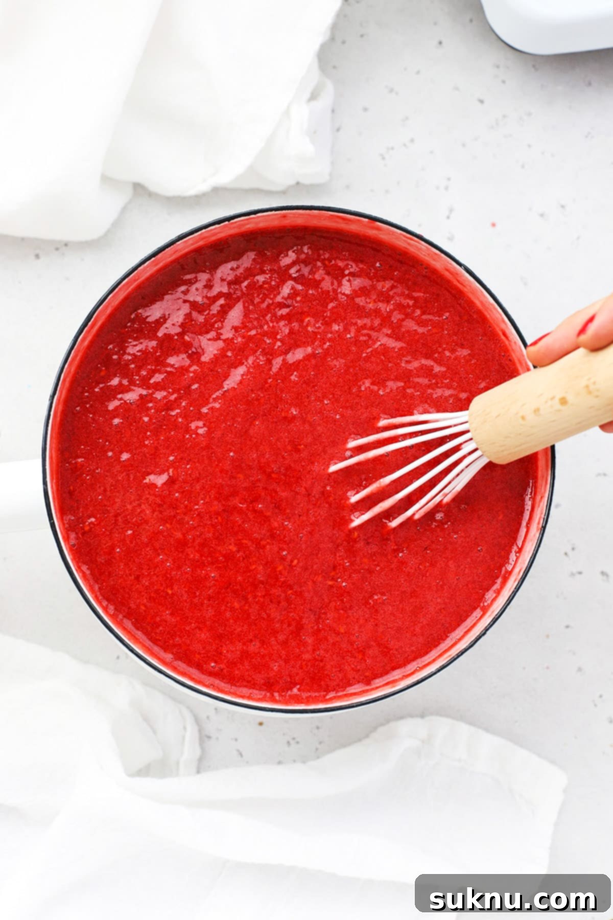 Whisking the raspberry jam vigorously in the saucepan to ensure all ingredients are well combined and the pectin activates.
