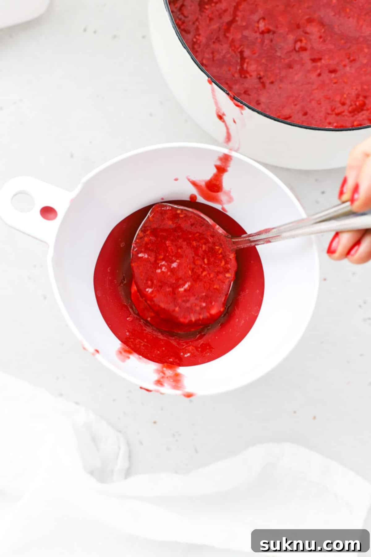Carefully spooning the warm raspberry freezer jam into clean, empty jars, preparing for storage.