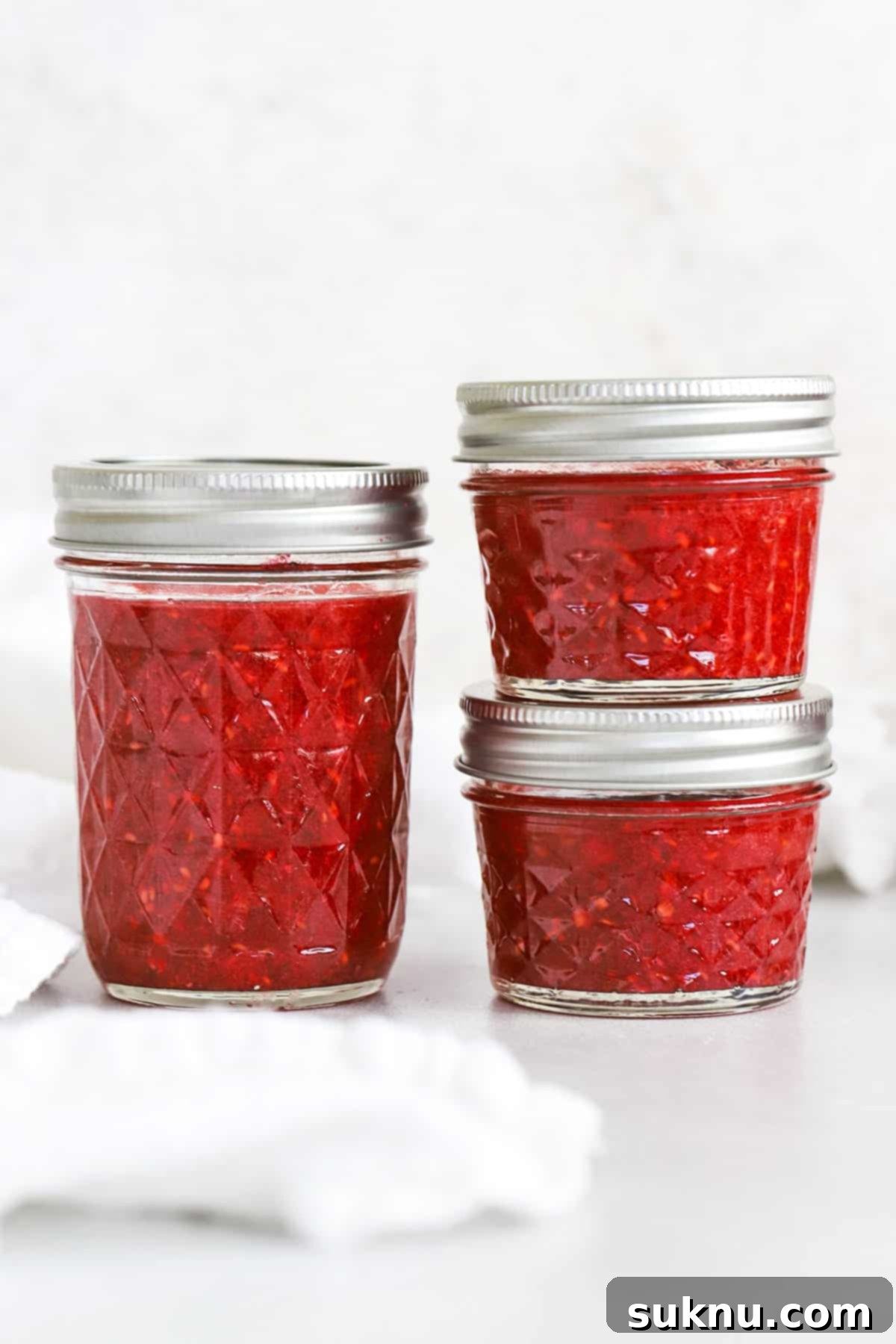 Front view of different sizes of jars filled with vibrant raspberry freezer jam, showcasing variety.
