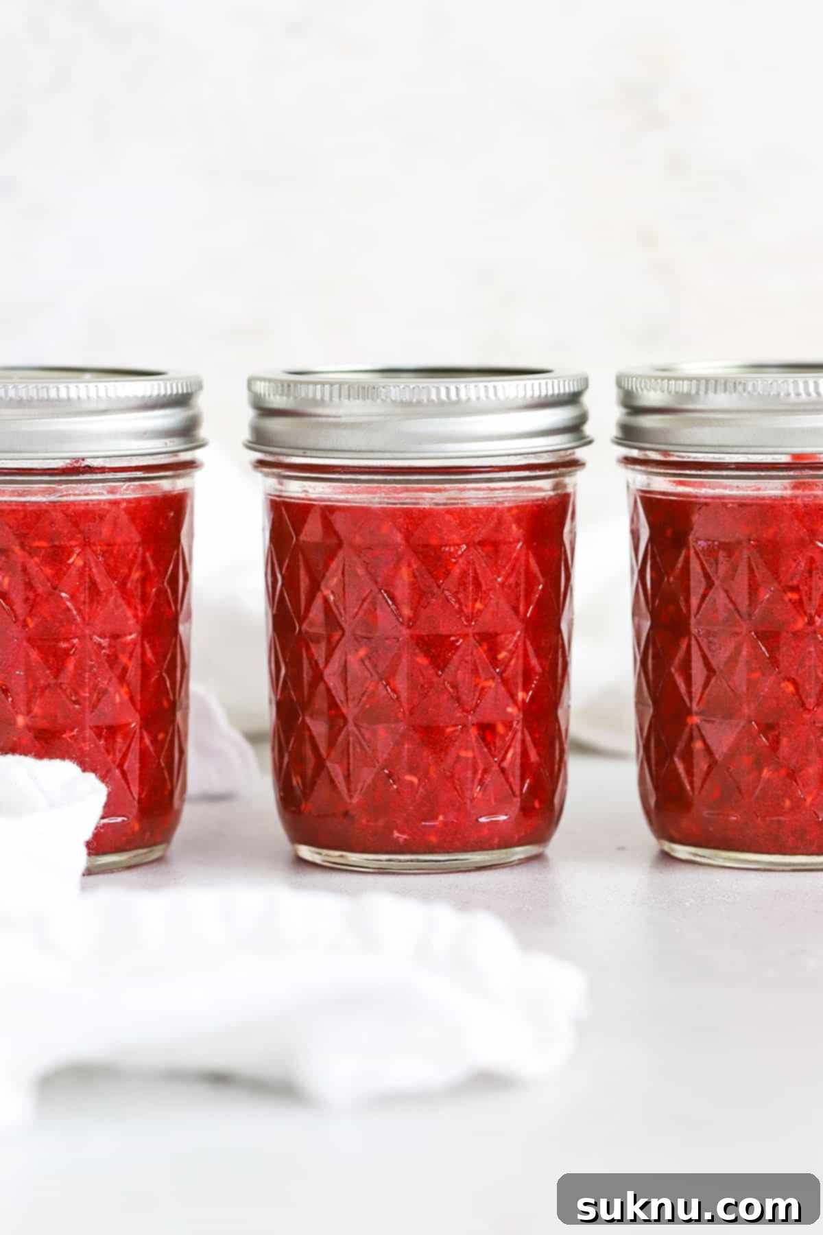 Front view of three jars of easy raspberry freezer jam, highlighting their homemade charm.