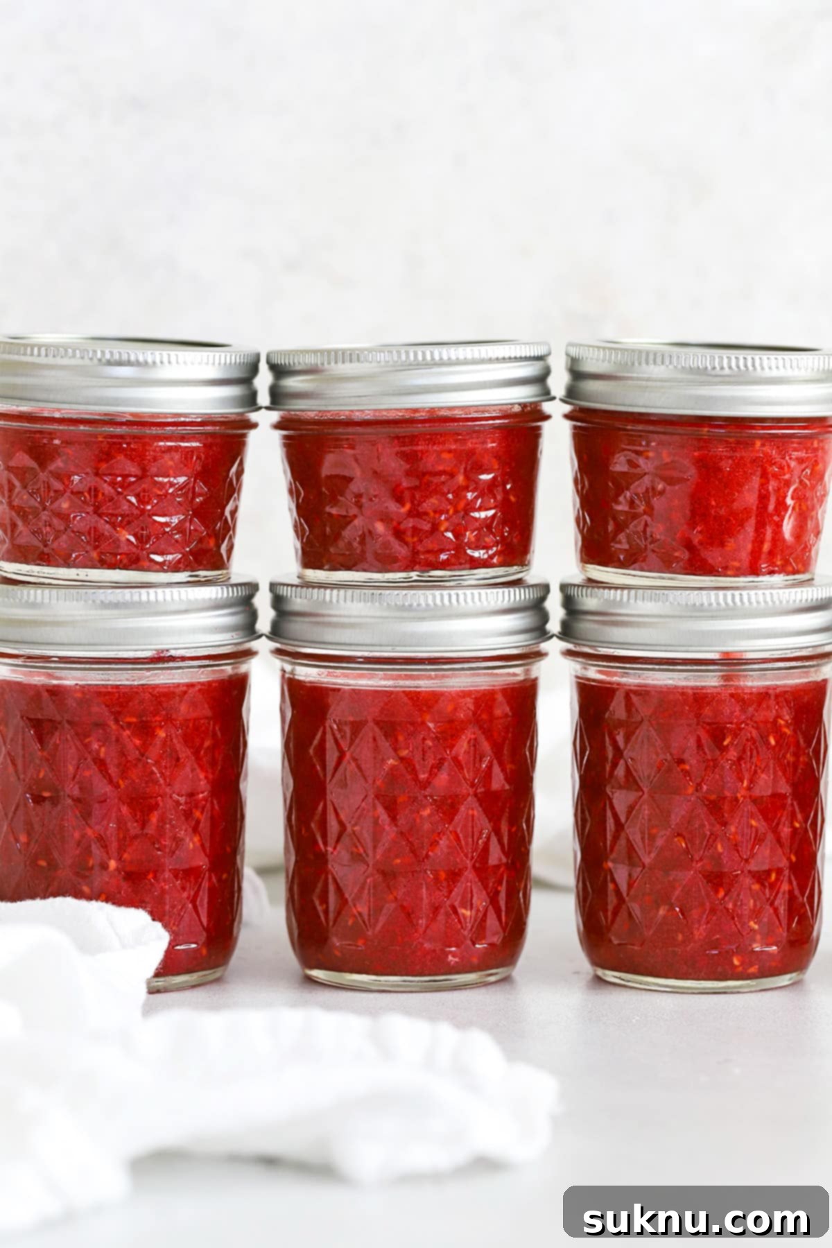 Front view of jars of low sugar raspberry freezer jam stacked neatly.