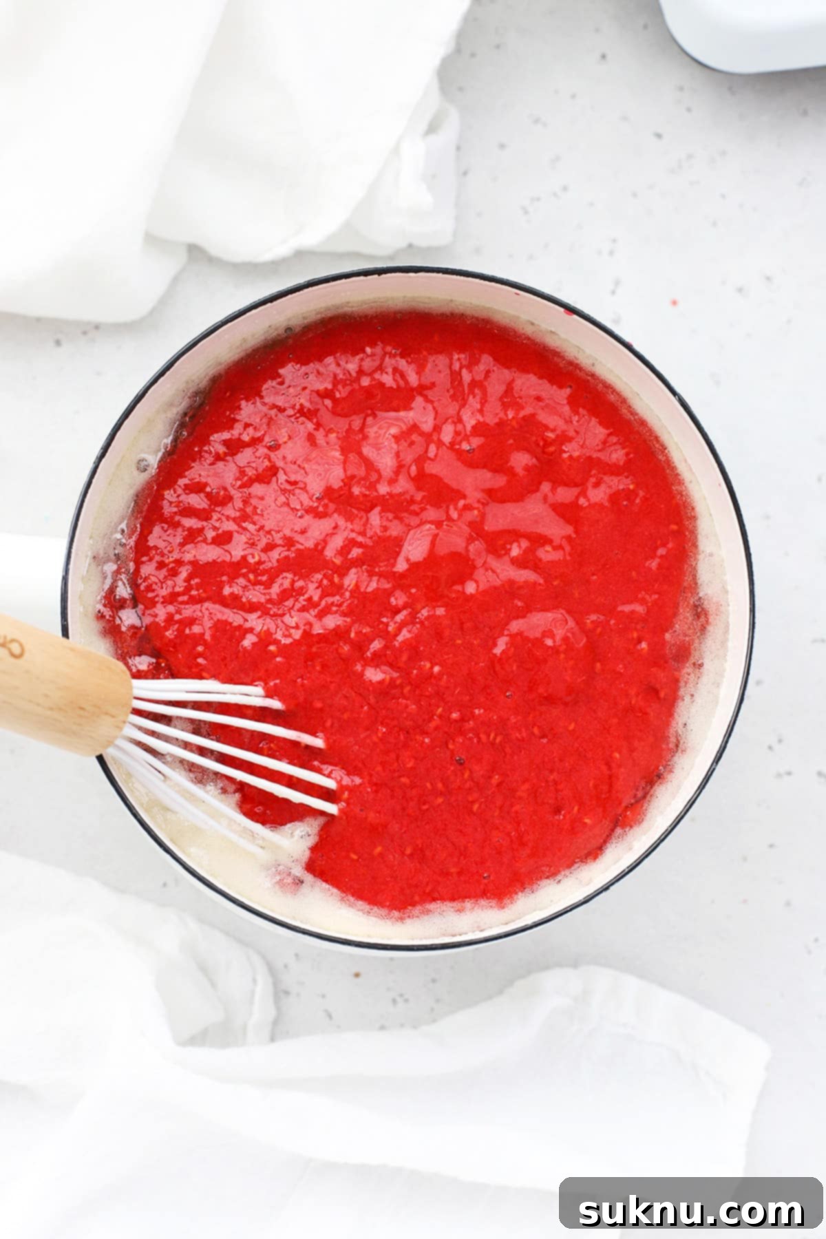 Incorporating mashed raspberries into the hot pectin and sugar mixture, stirring to combine for freezer jam.